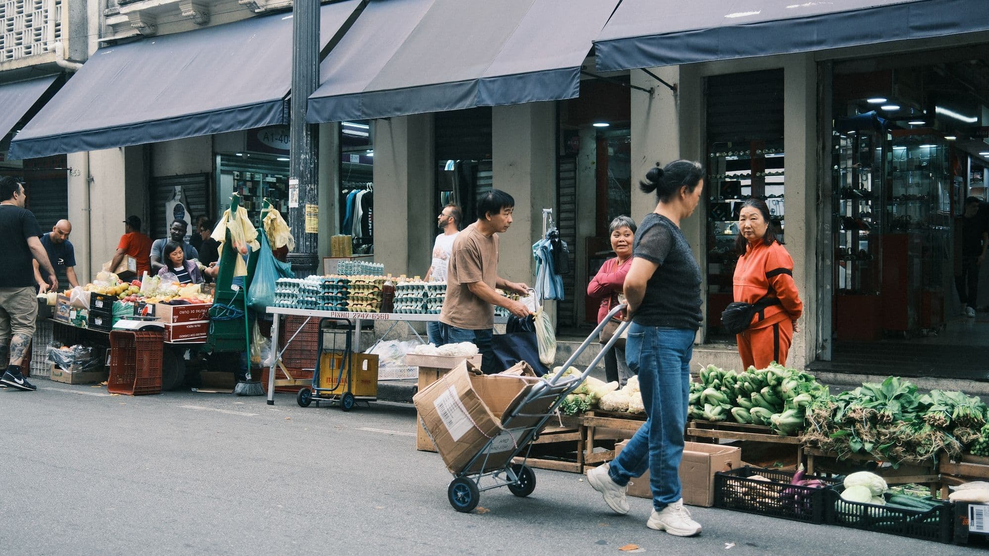 Shoppers moving between fruit and vegetable stalls at a São Paulo street market.