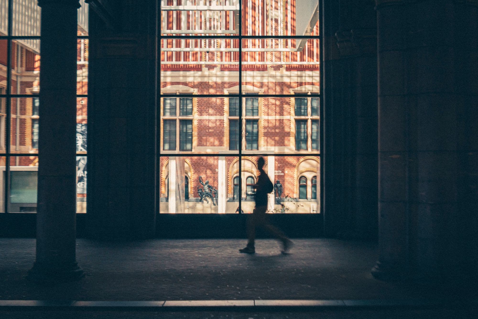 A person walks through a grand museum hall toward an open city view.