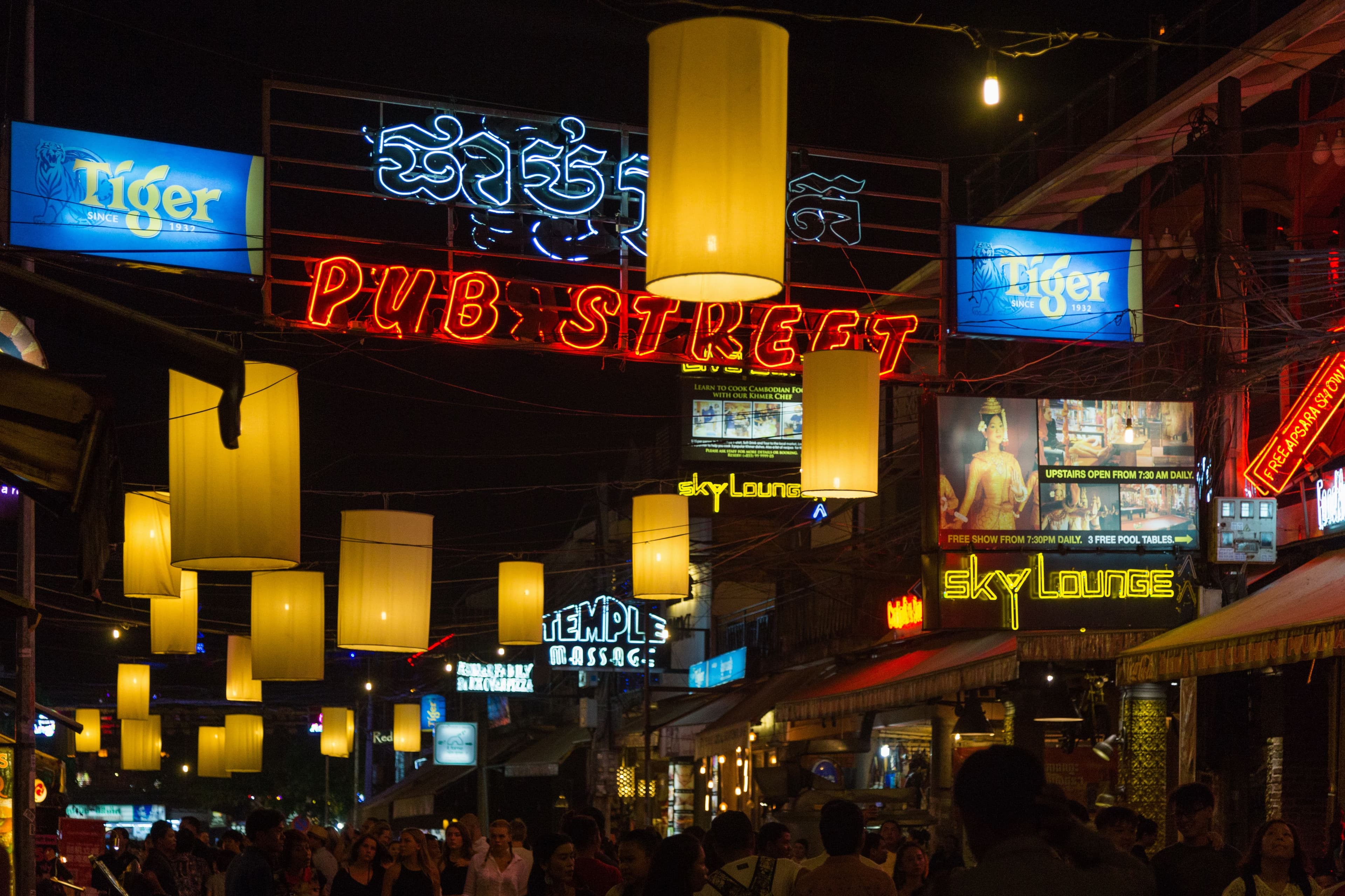 Red neon Pub Street sign and yellow paper lanterns over a crowded street of bars at night in Siem Reap.