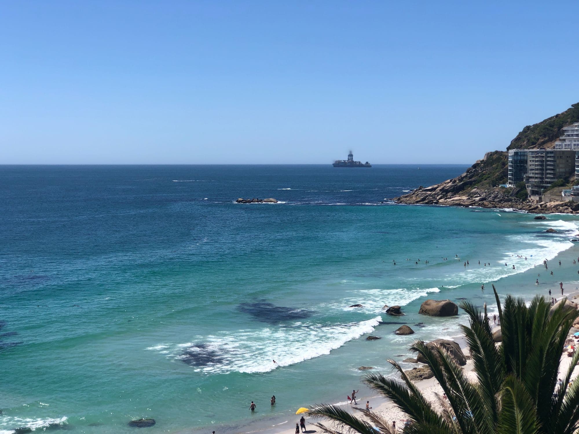 Turquoise water and white sand at Clifton in Cape Town, with granite boulders and a ship on the horizon.