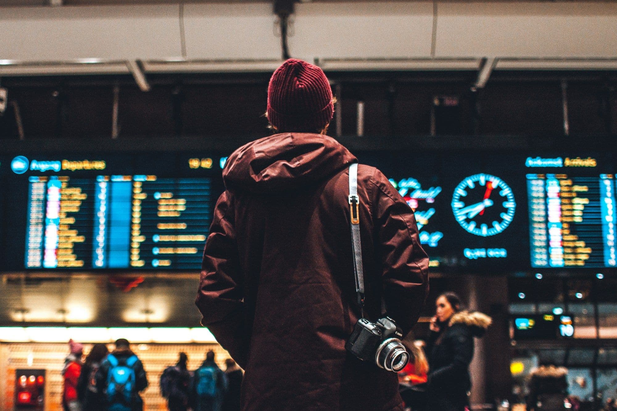 A traveler reading a flight-information board inside an airport terminal.