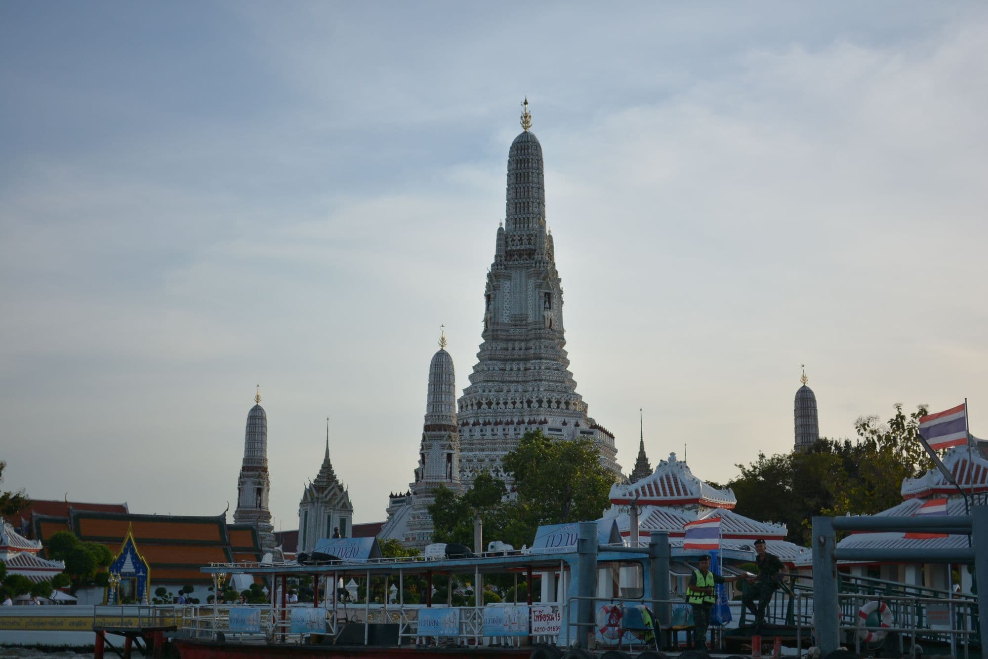 The tall ornate spire of Wat Arun on the bank of the Chao Phraya River in Bangkok at dusk.