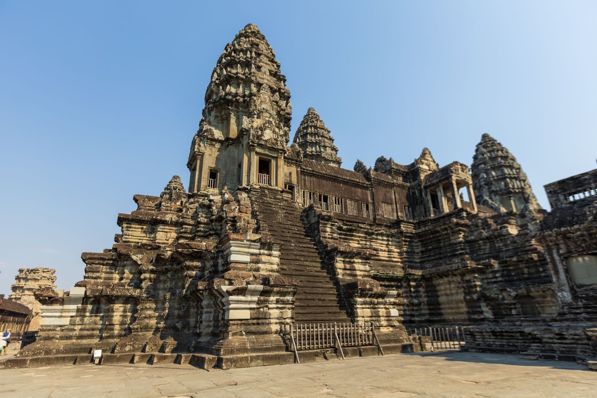The weathered stone towers and steep stairways of Angkor Wat's upper level against a clear blue sky.