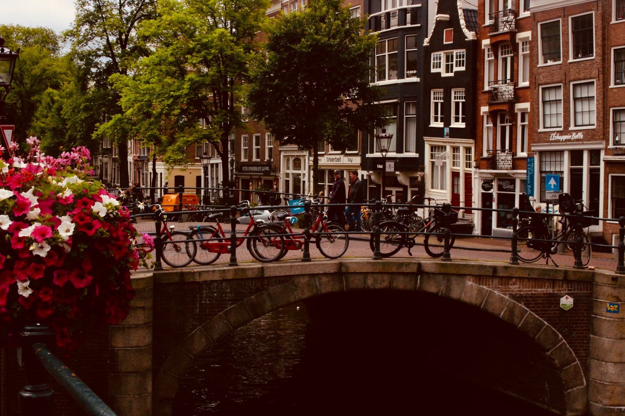 Bicycles line a flower-covered bridge above an Amsterdam canal.