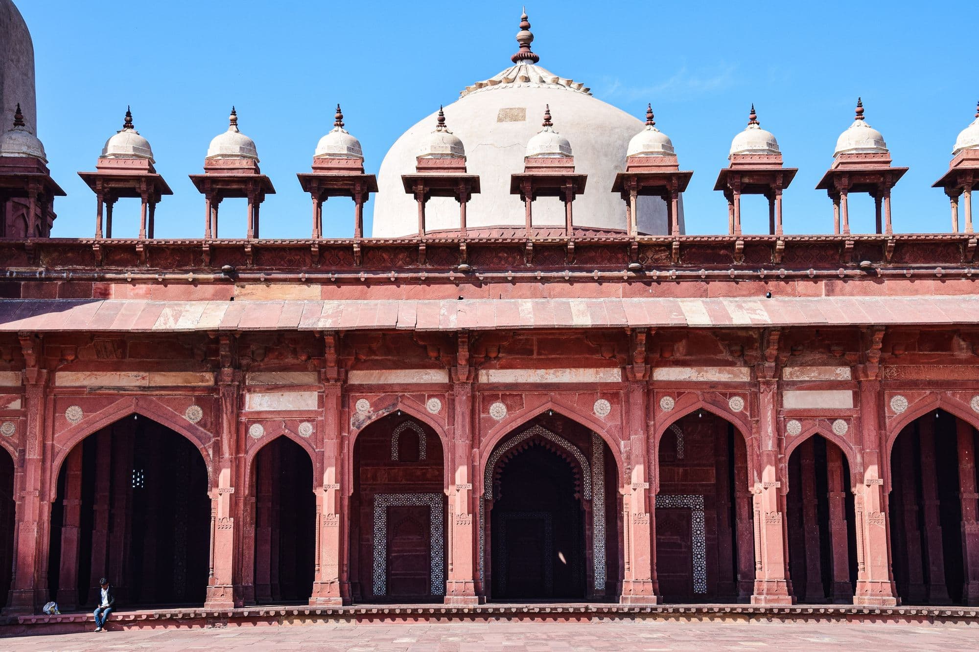 The long arcade of red sandstone arches and white domed kiosks around the courtyard of the Jama Masjid at Fatehpur Sikri.