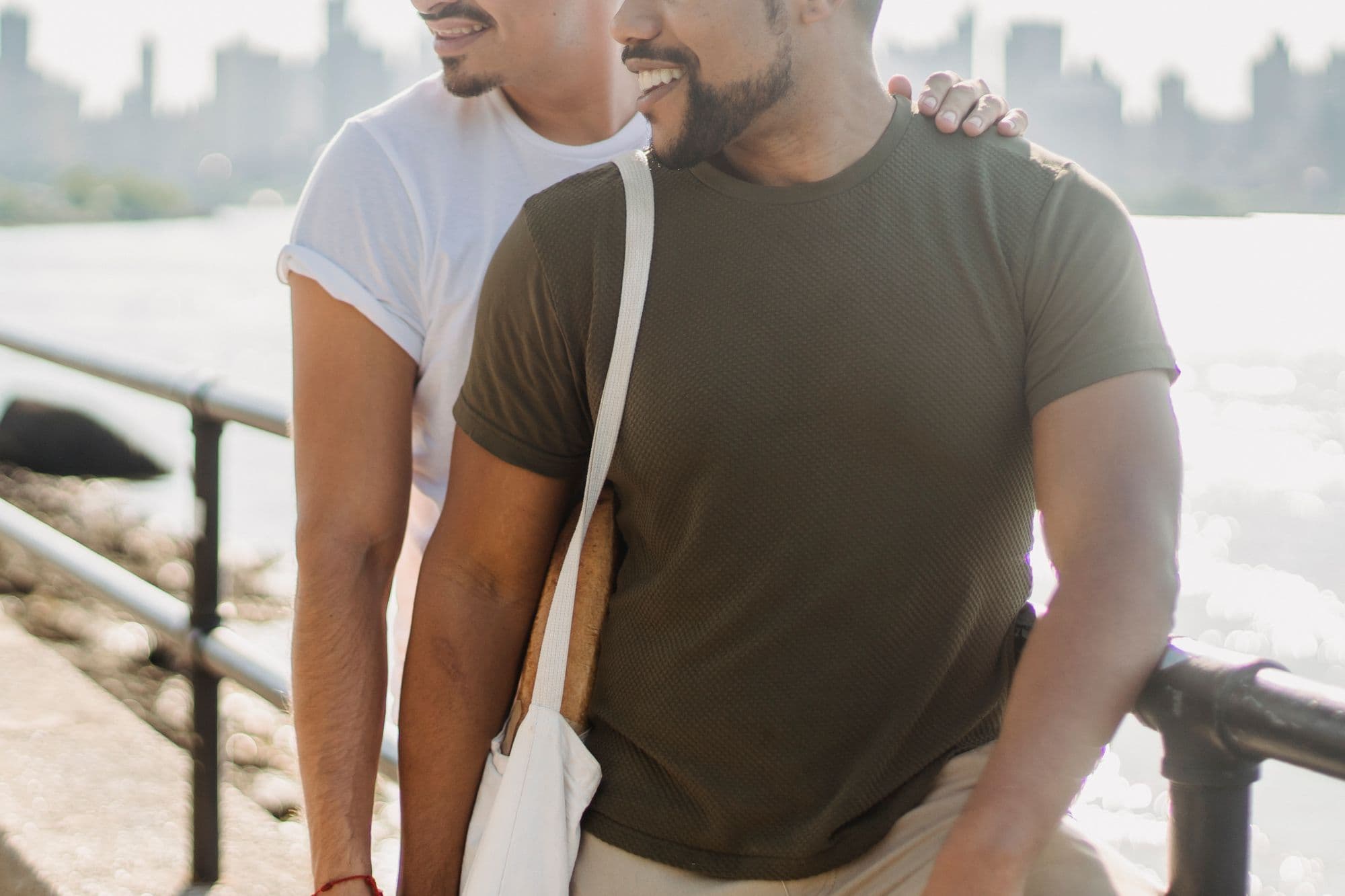 Two men sitting together on a waterfront promenade on a clear day.