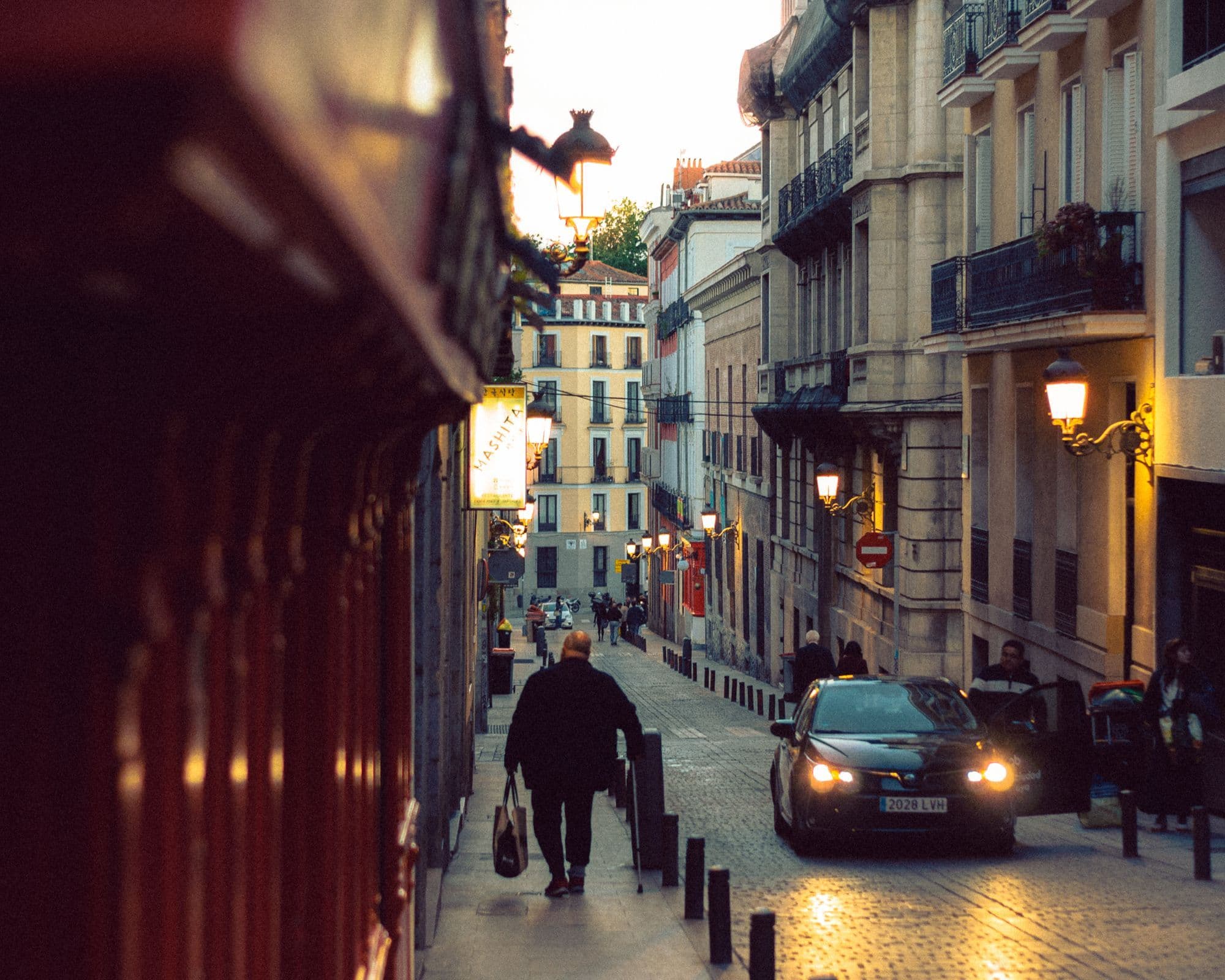 A pedestrian walking along a cobbled Madrid street at twilight.