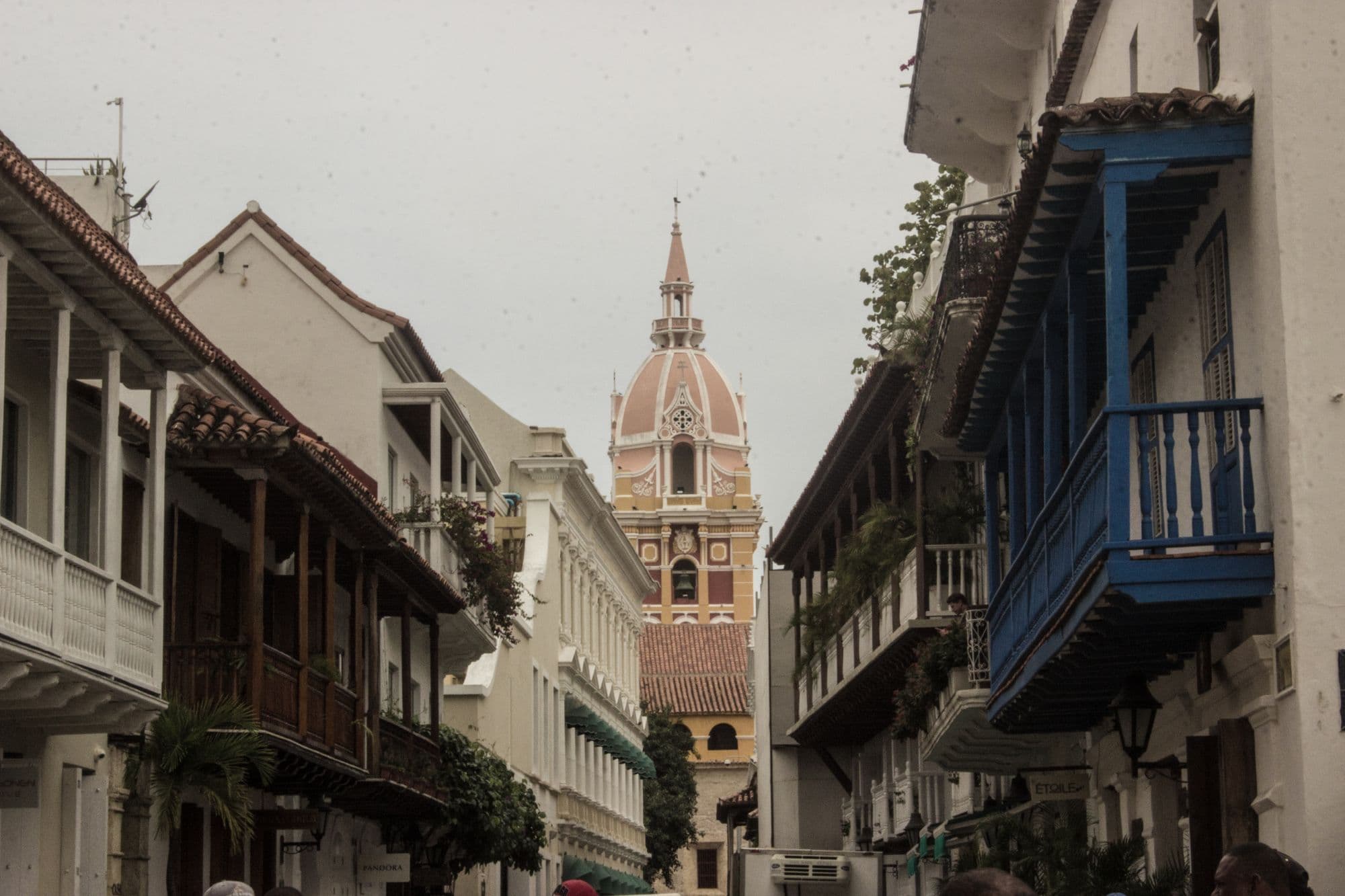 A narrow colonial street in Cartagena's walled city with wooden balconies and the domed cathedral tower at the end.