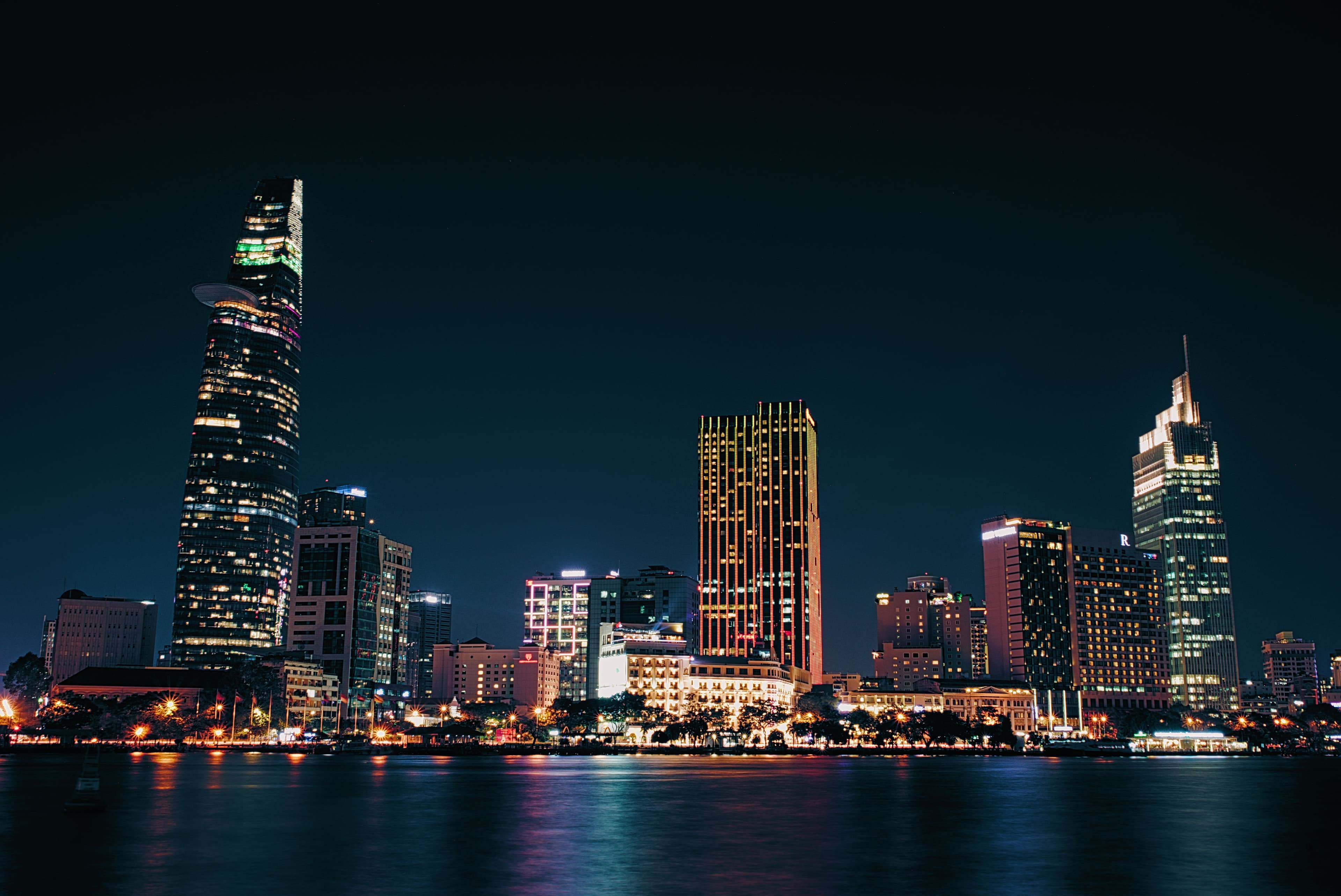 The Ho Chi Minh City skyline lit up at night across the Saigon River, with the Bitexco tower on the left.