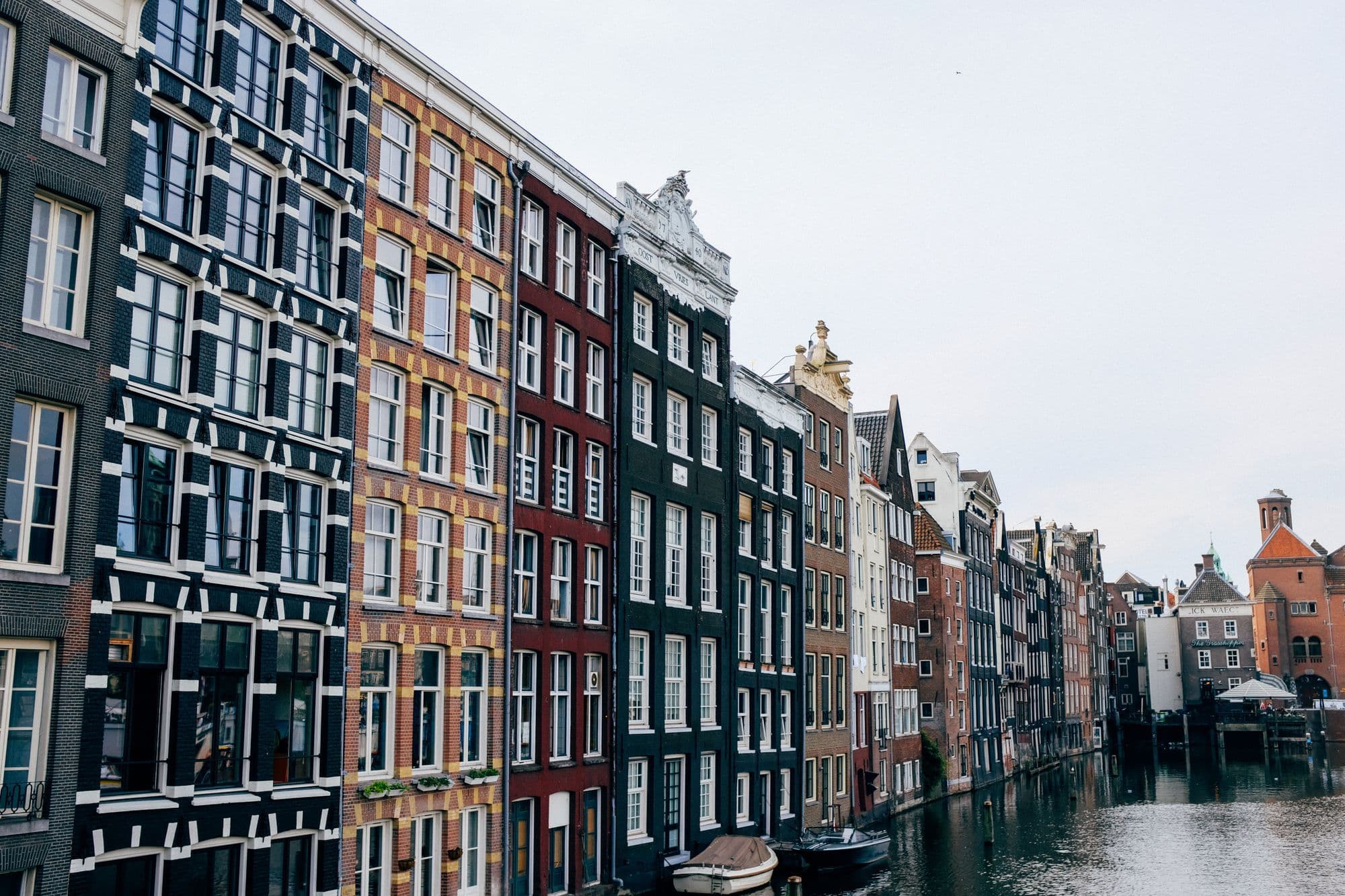 Narrow Amsterdam canal houses and small boats line a sunlit canal.
