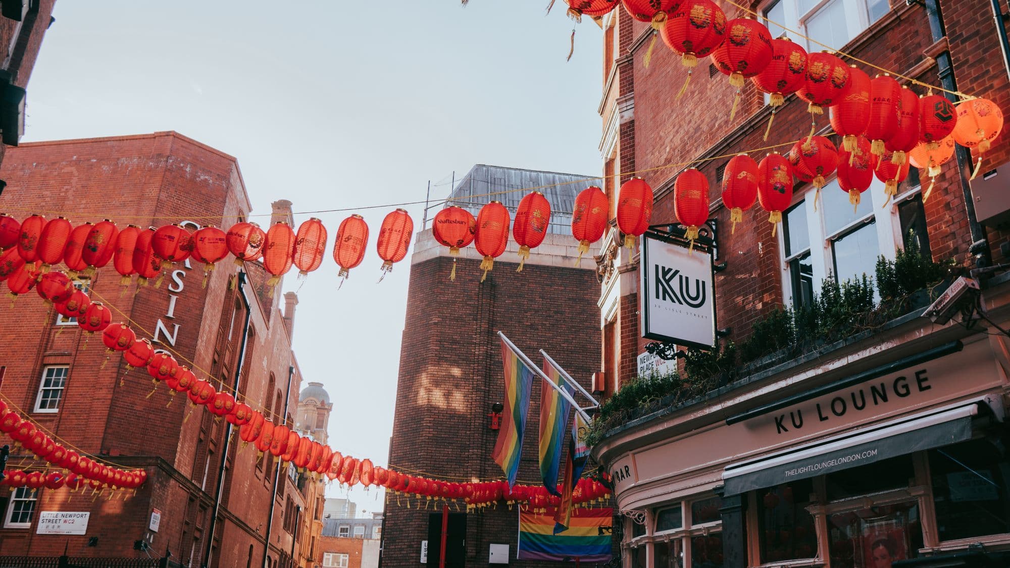 Rainbow flags and red lanterns hanging above a busy central London street.