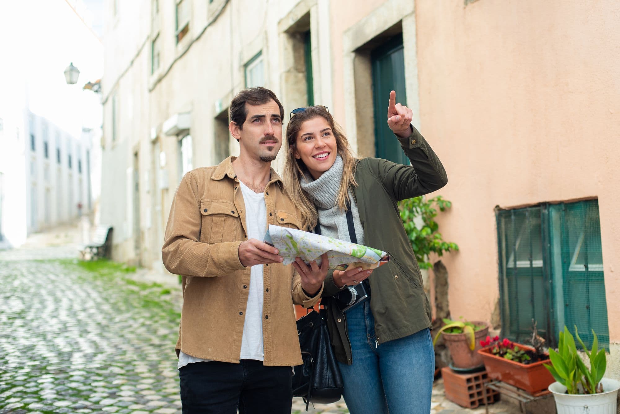 A smiling couple looks at a paper map together on a European old-town street.