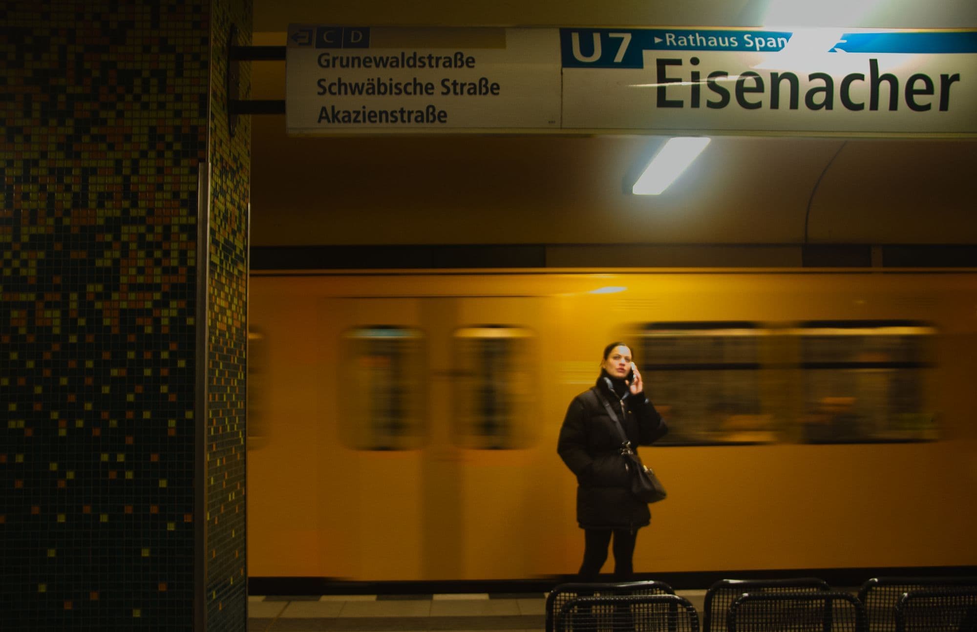 A passenger waiting as a Berlin U-Bahn train blurs through Eisenacher Straße station.