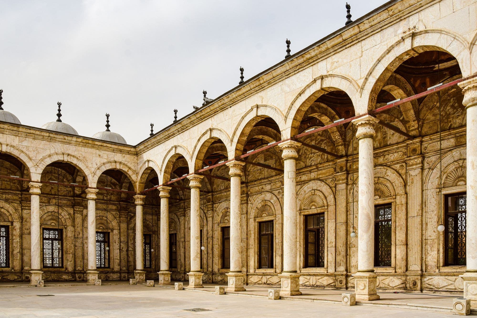 A courtyard of white alabaster arches and columns with small domes above at the Mosque of Muhammad Ali in the Citadel.