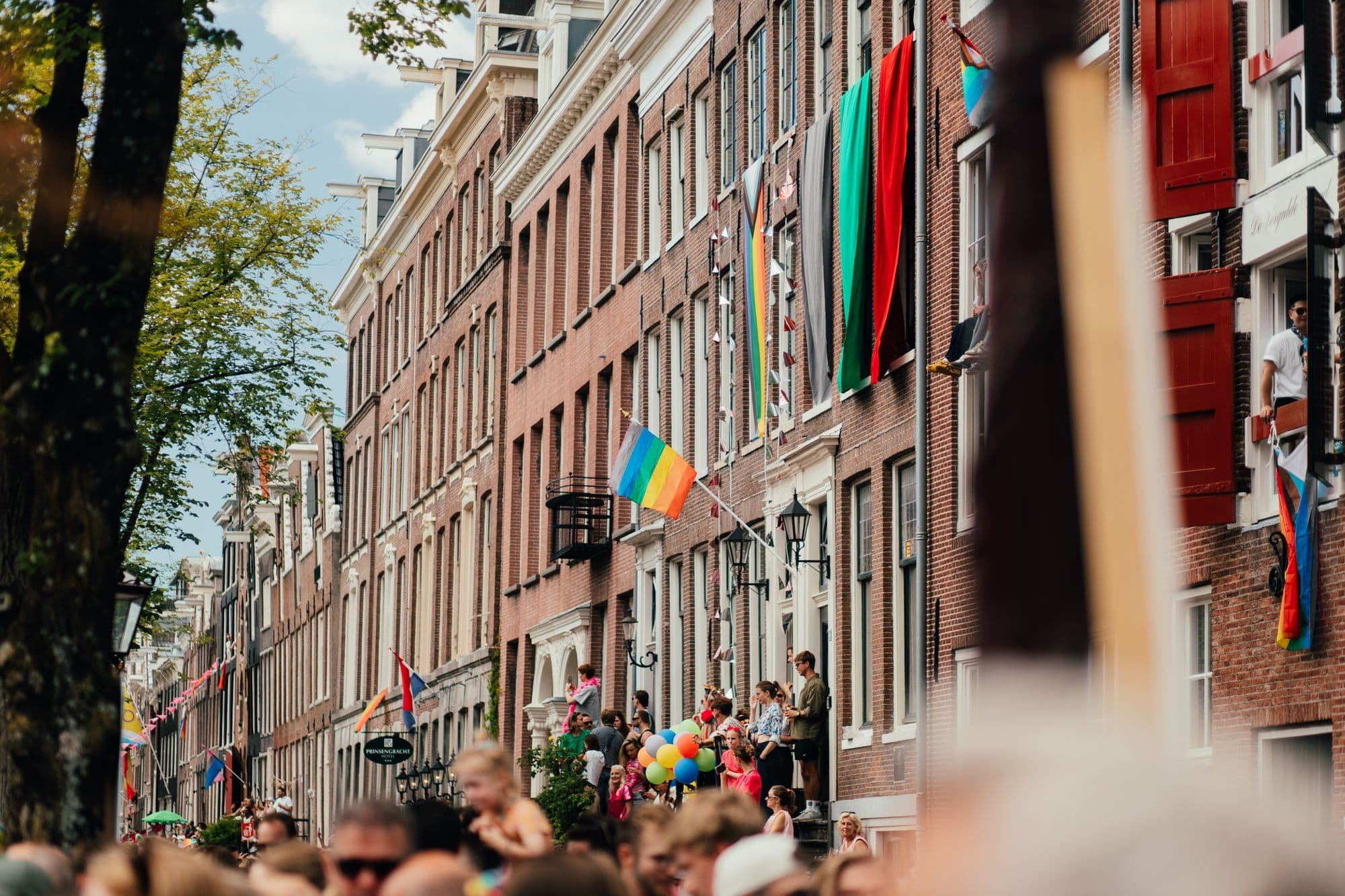 Rainbow flags above a crowded Amsterdam street during Pride.