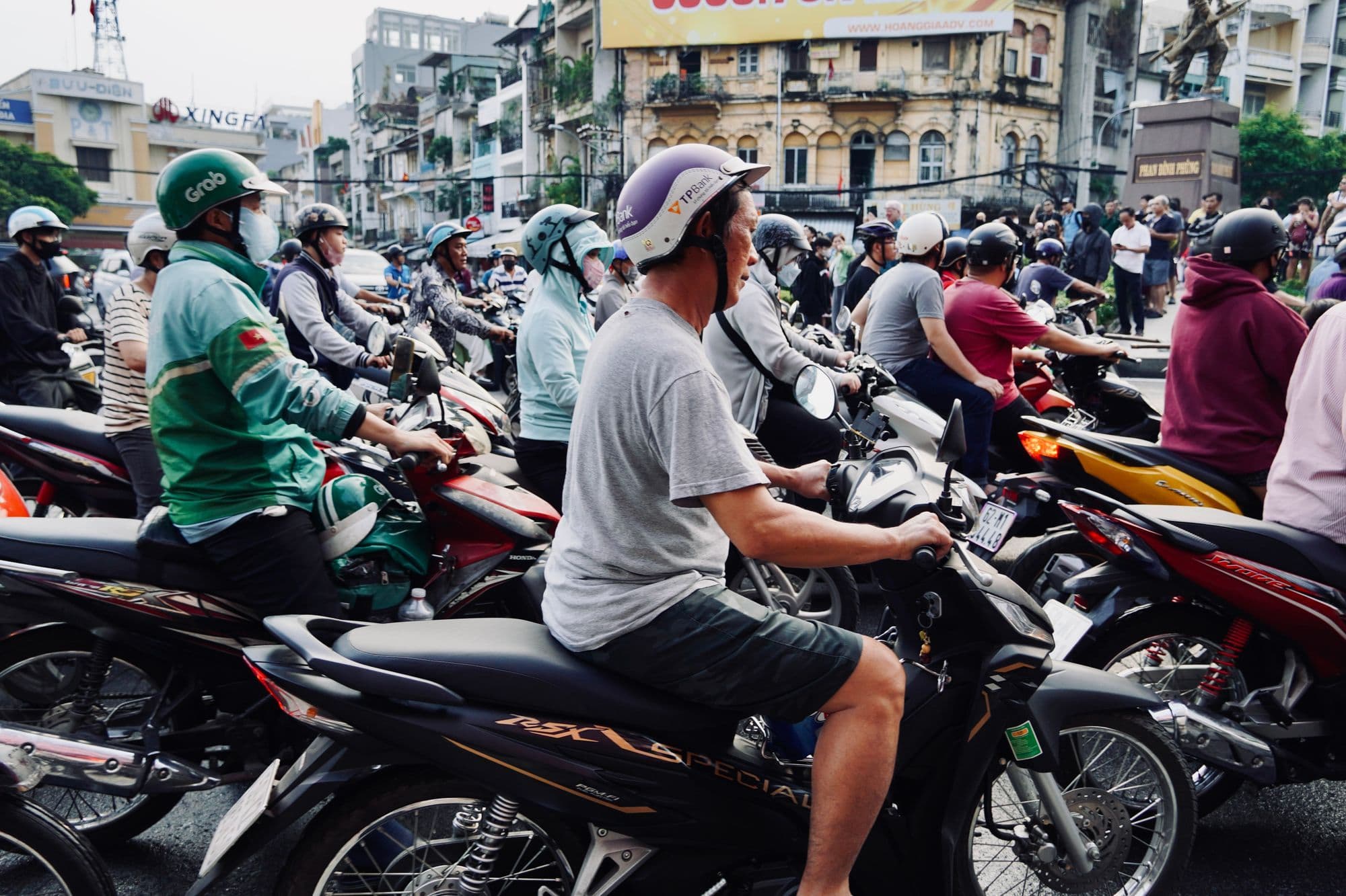 Rows of motorbike riders in helmets waiting at a traffic light on a busy street in Ho Chi Minh City.