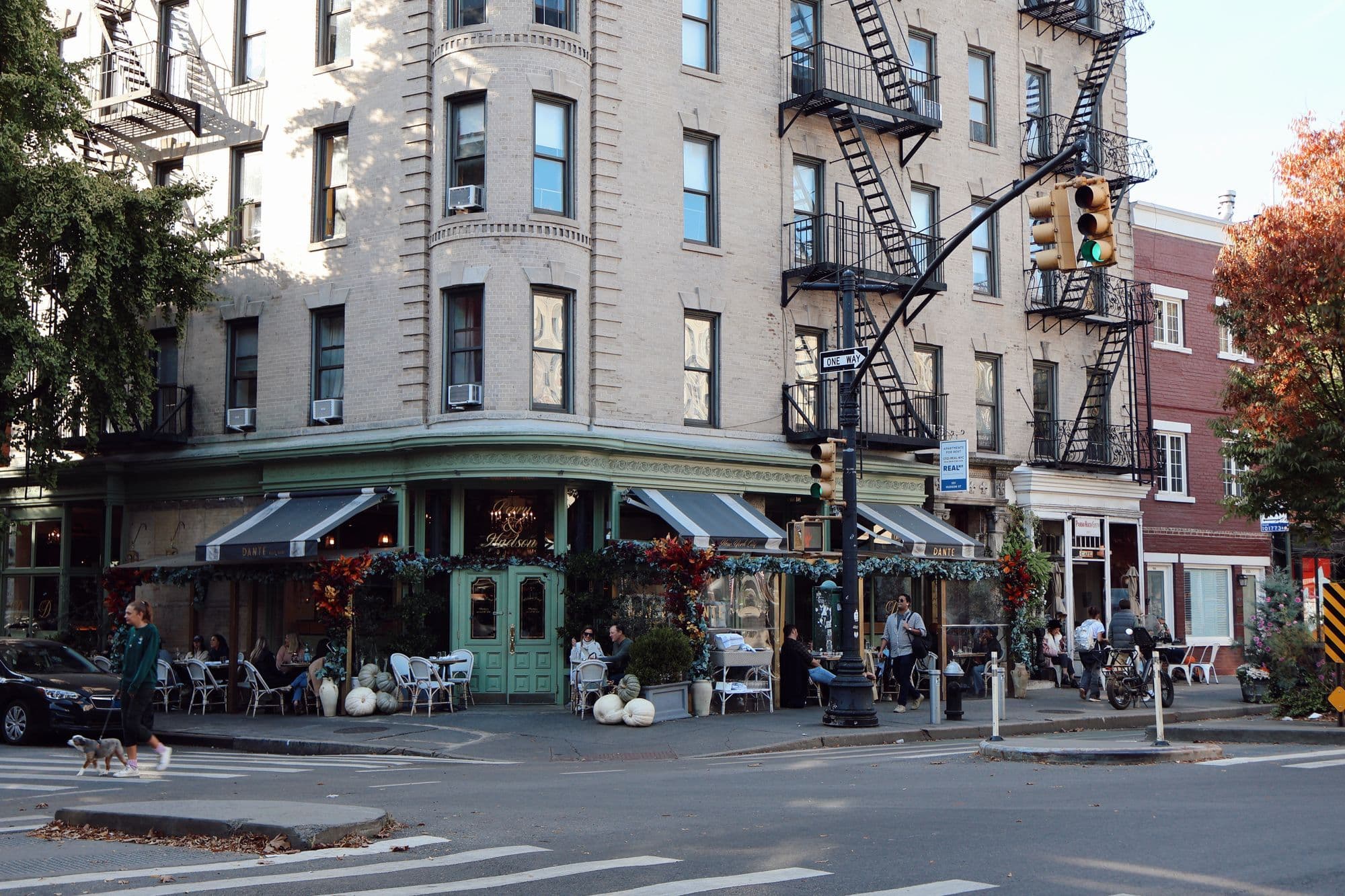 Outdoor café tables on a leafy New York City street corner.