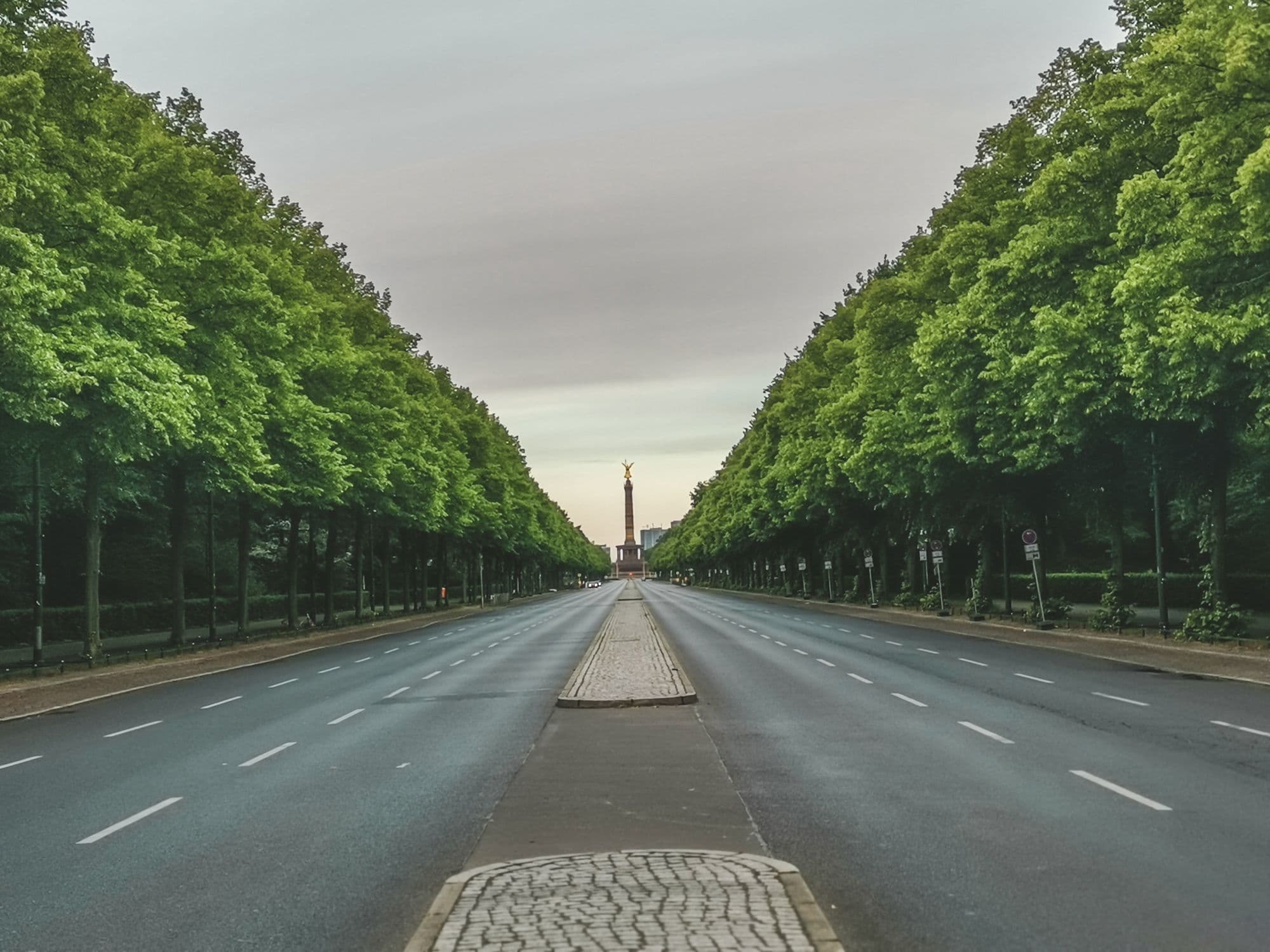 A straight tree-lined avenue leads toward a monument in Berlin's Tiergarten.