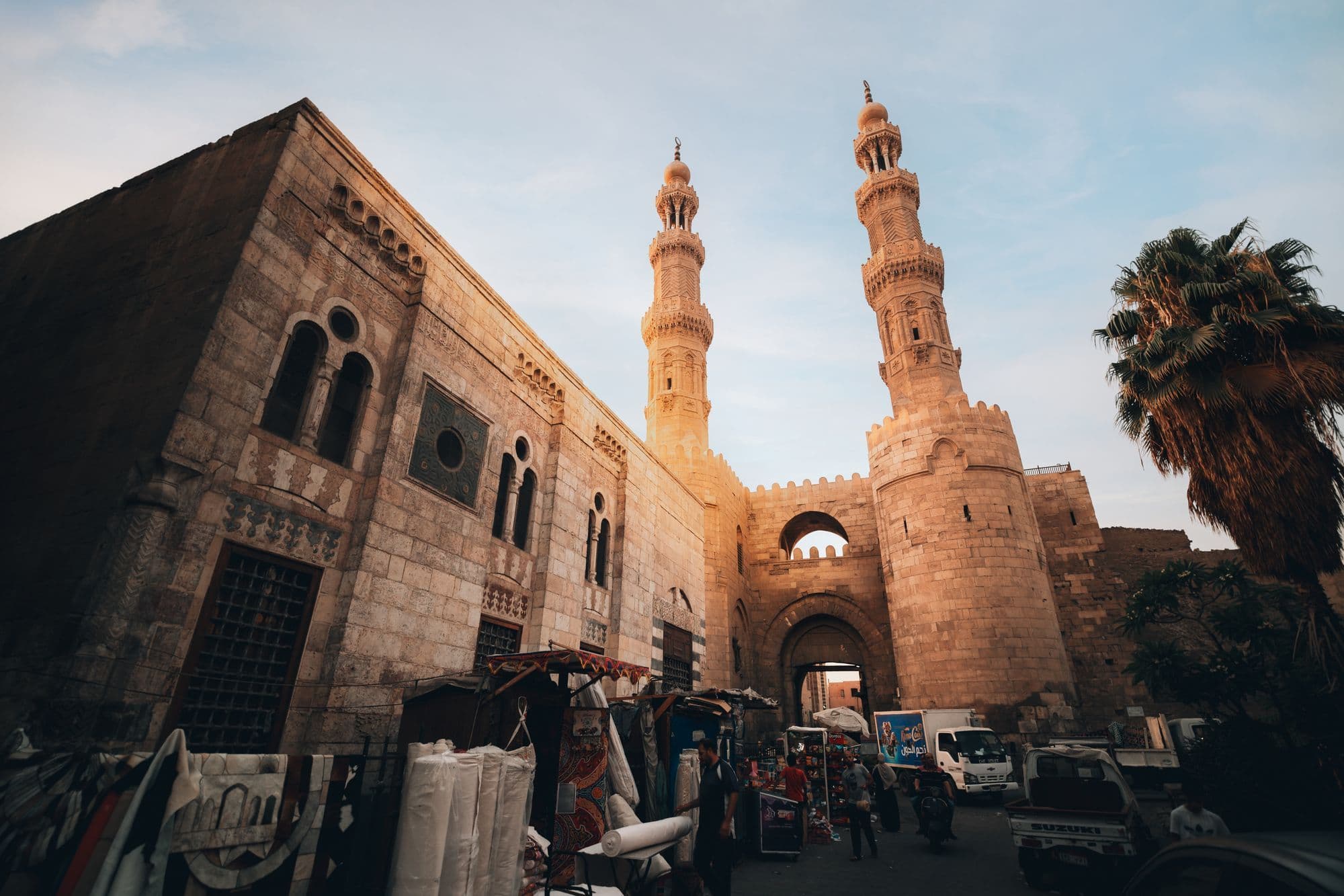 The twin minarets of Bab Zuweila above a stone gateway, with market stalls and people in the street below.