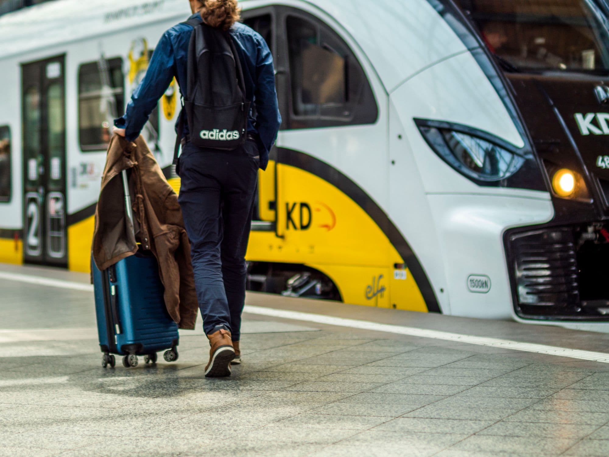 A traveler with a suitcase waits beside a train at a station platform.