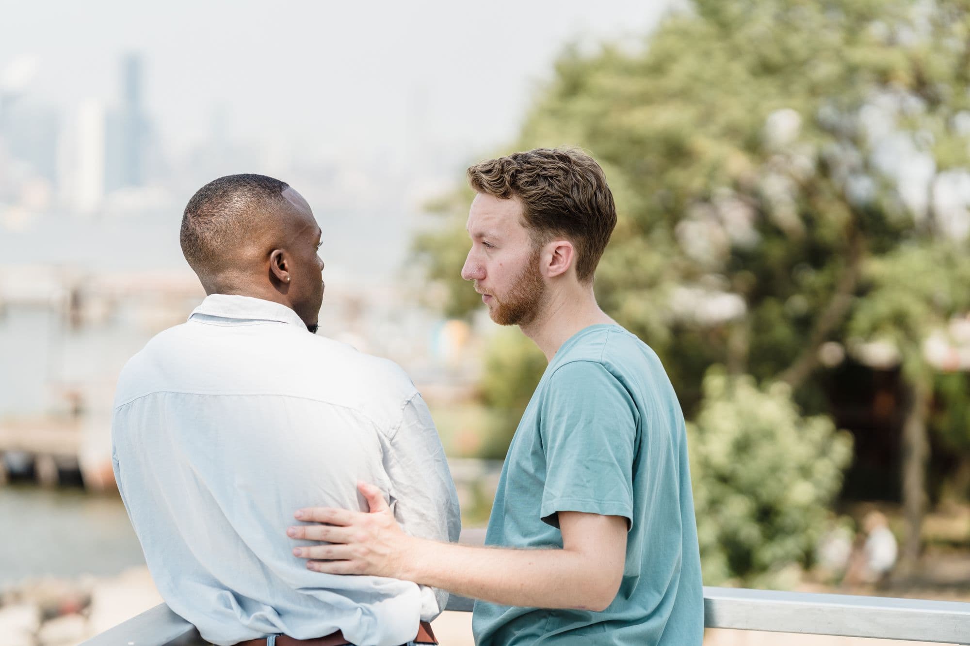 An interracial couple embraces at a city waterfront in warm evening light.