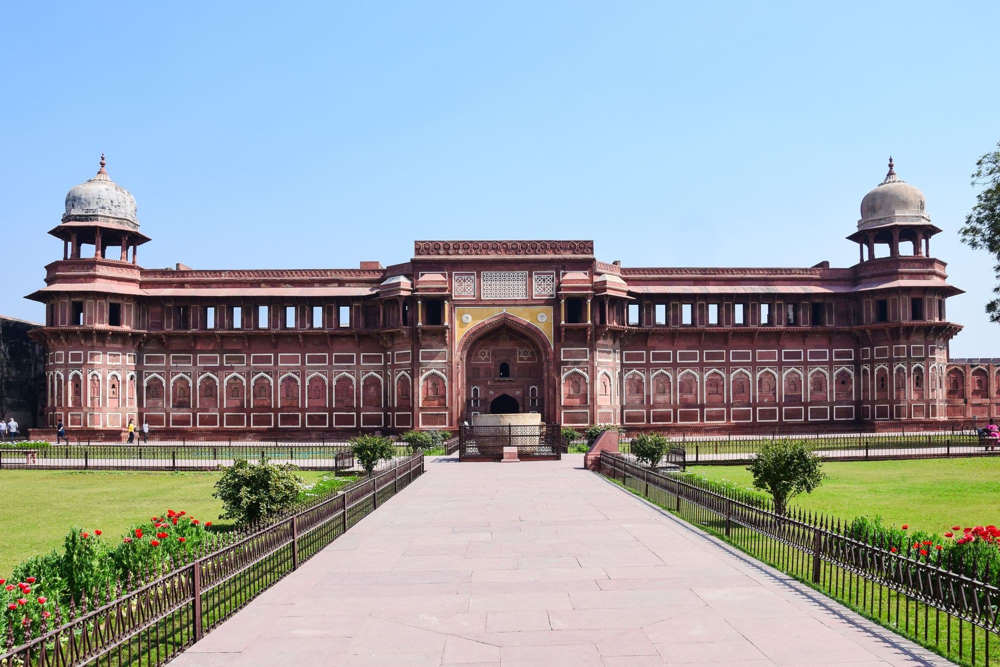 The red sandstone facade of the Jahangiri Mahal inside Agra Fort, with domed towers at each corner and a lawn in front.
