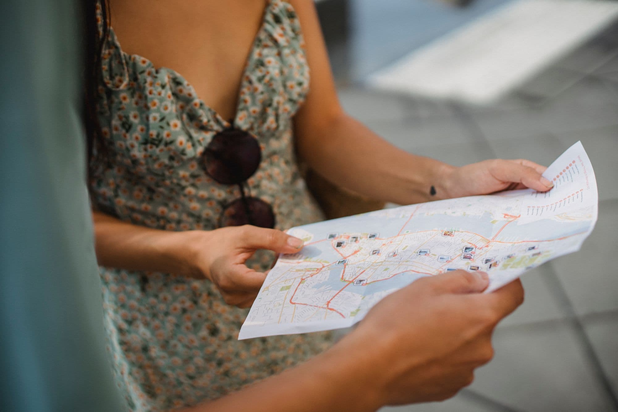 A couple in summer clothes looks at a paper map while walking through a city.