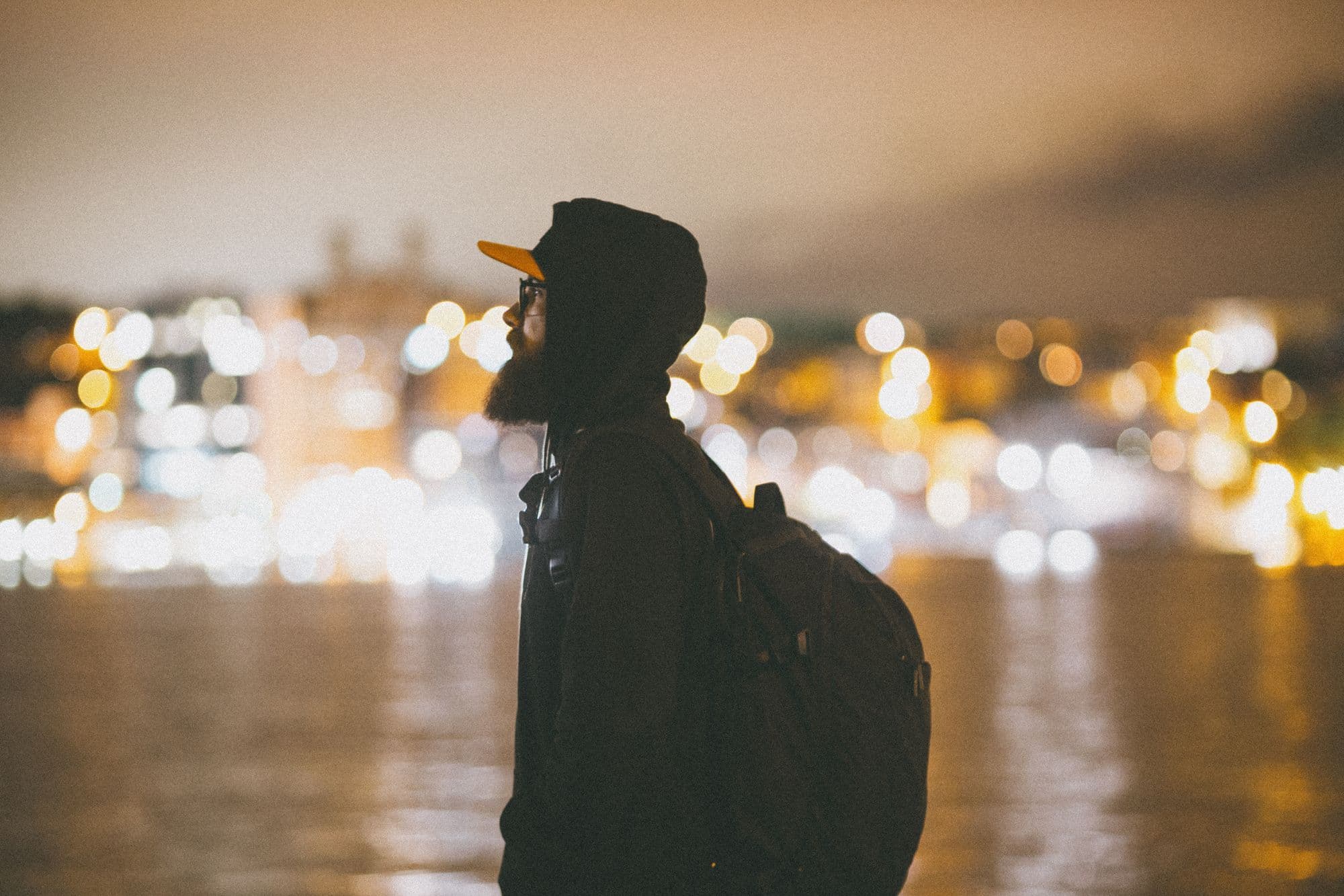 A traveler with a backpack standing near city lights after dark.