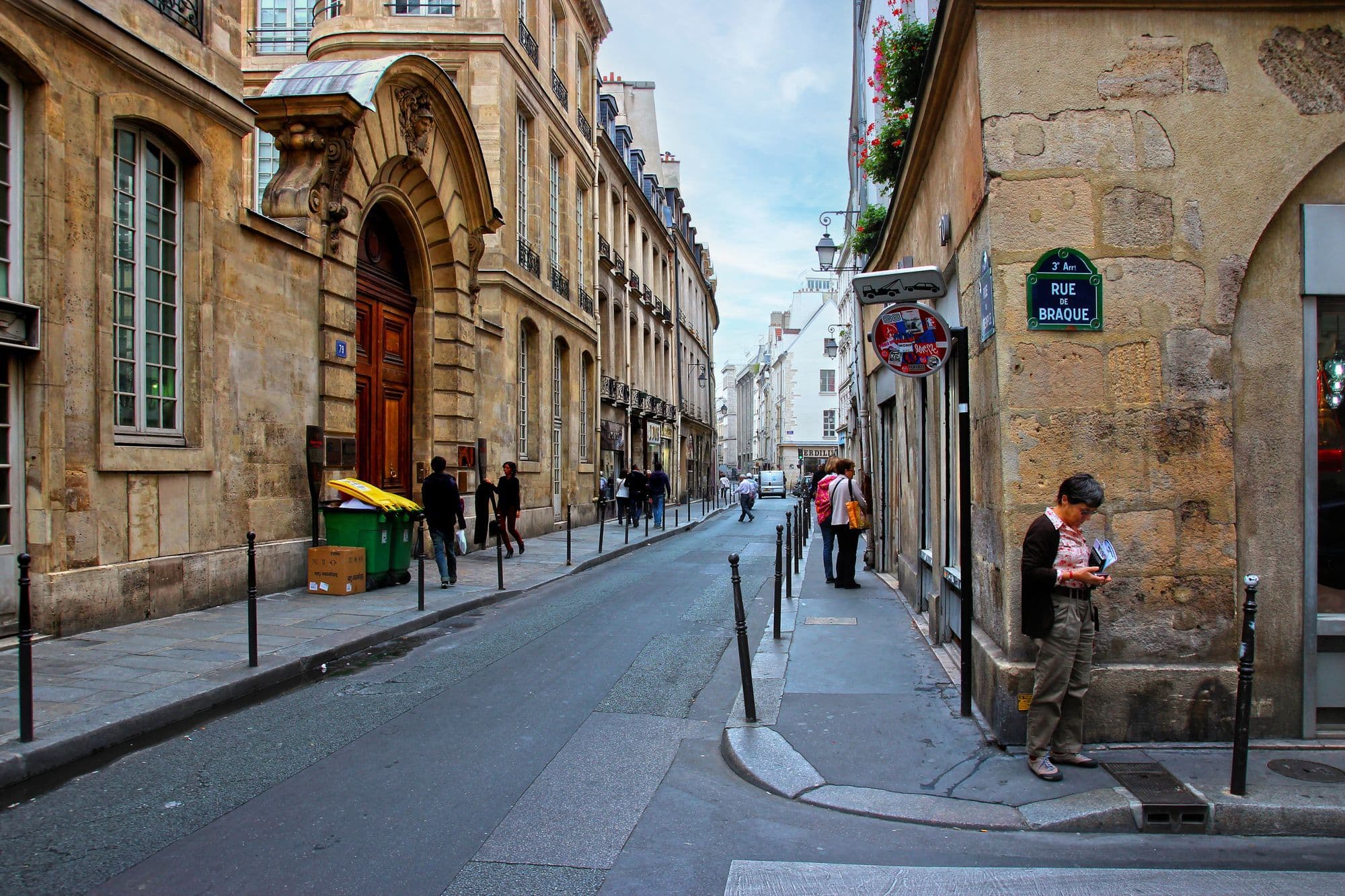 Pedestrians pass pale stone buildings and shopfronts on Rue Braque in Le Marais.