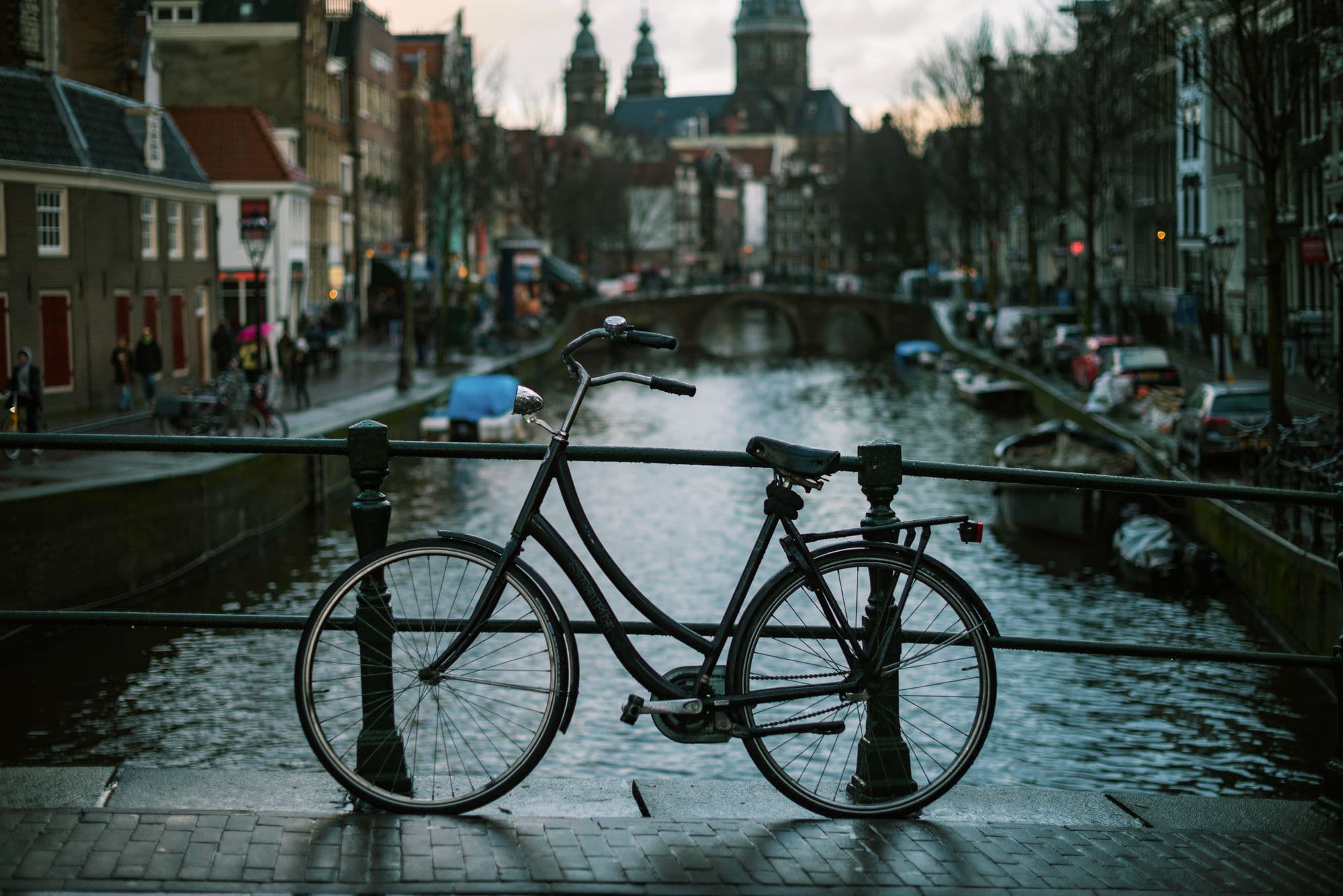 A bicycle is parked against railings beside an Amsterdam canal bridge.