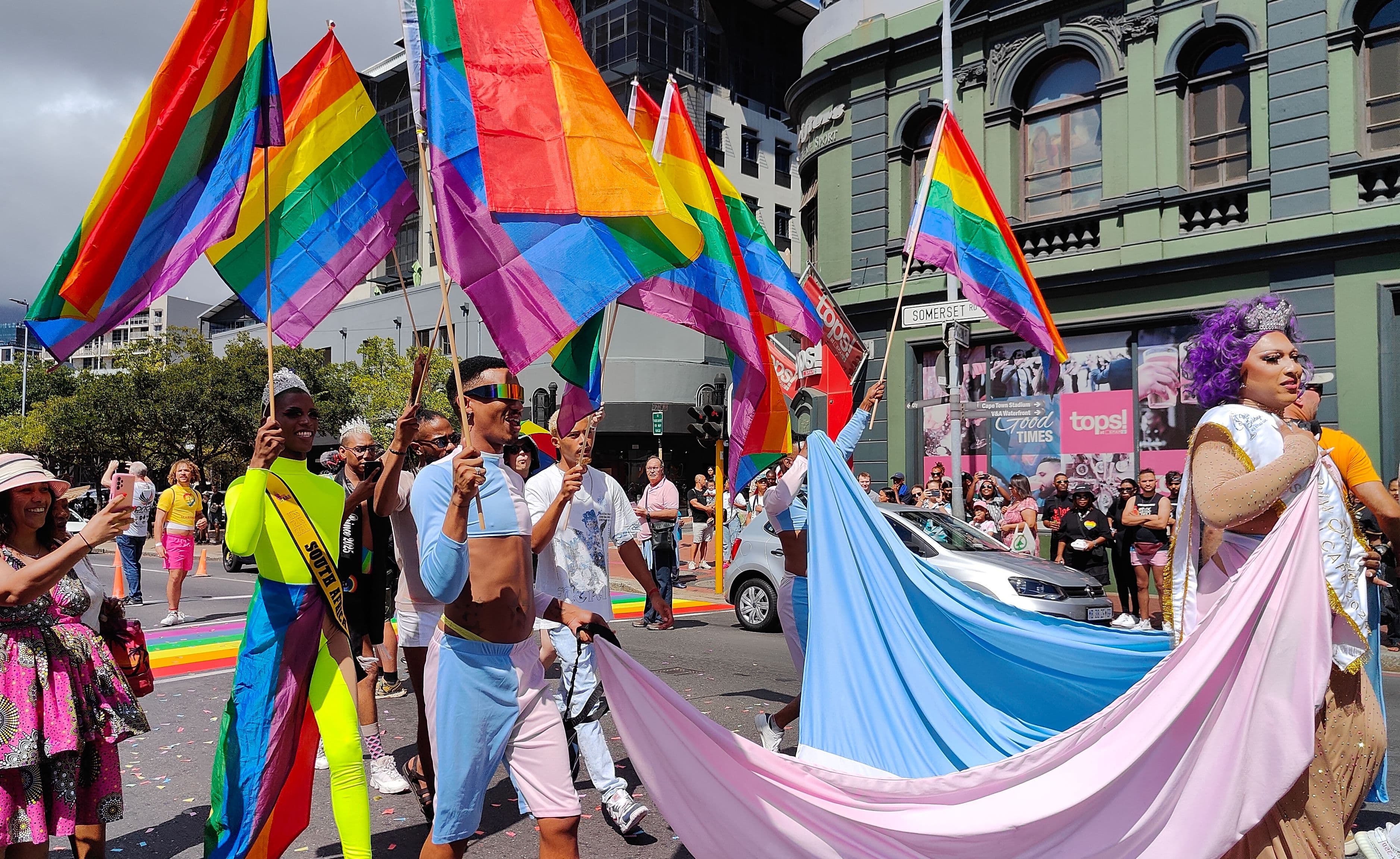 Marchers carrying large rainbow and Pride flags along a street lined with Victorian buildings at Cape Town Pride 2025.