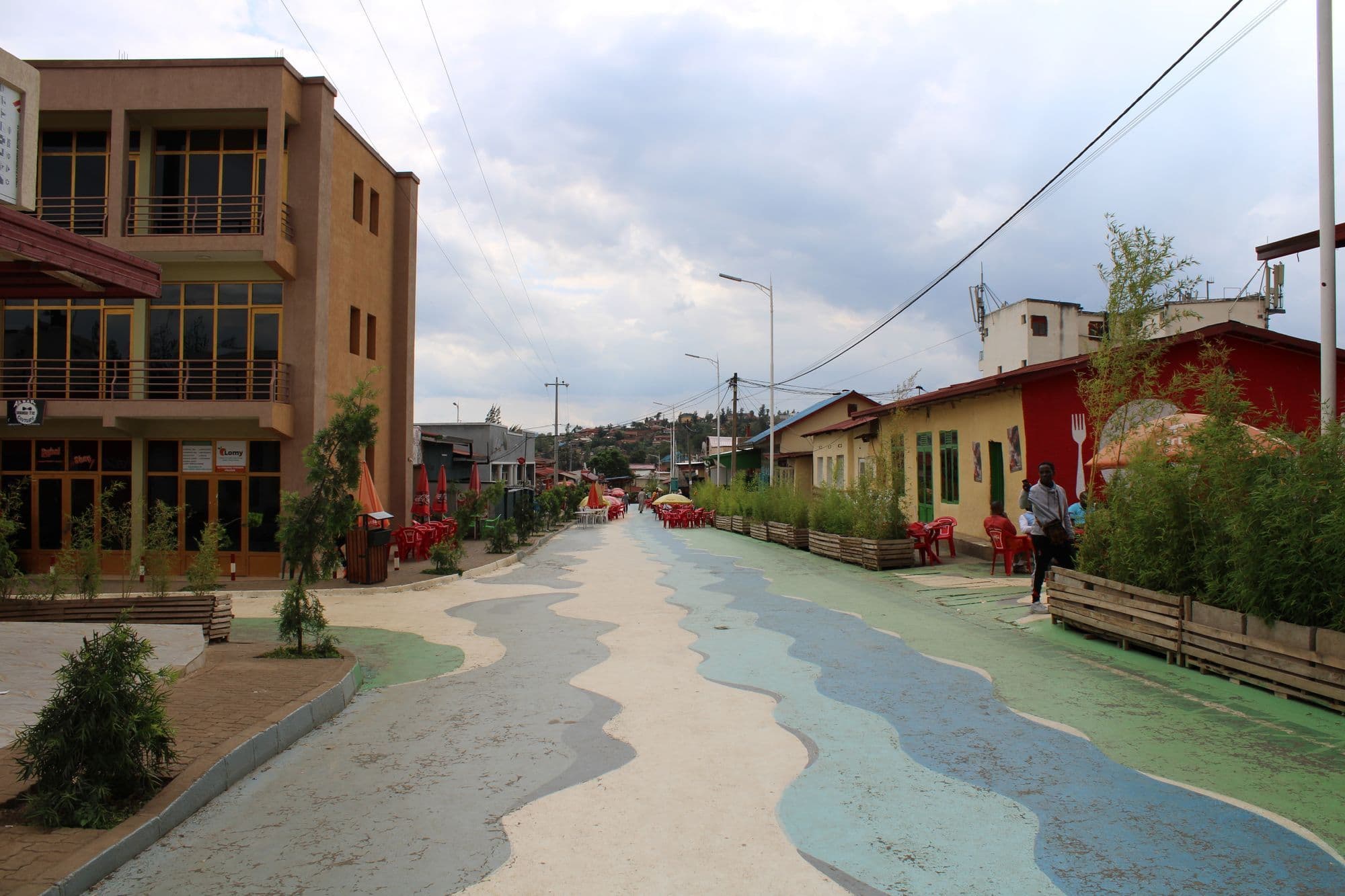 A car-free street in Nyamirambo, Kigali, painted with flowing blue and green patterns, lined with shops and planters.