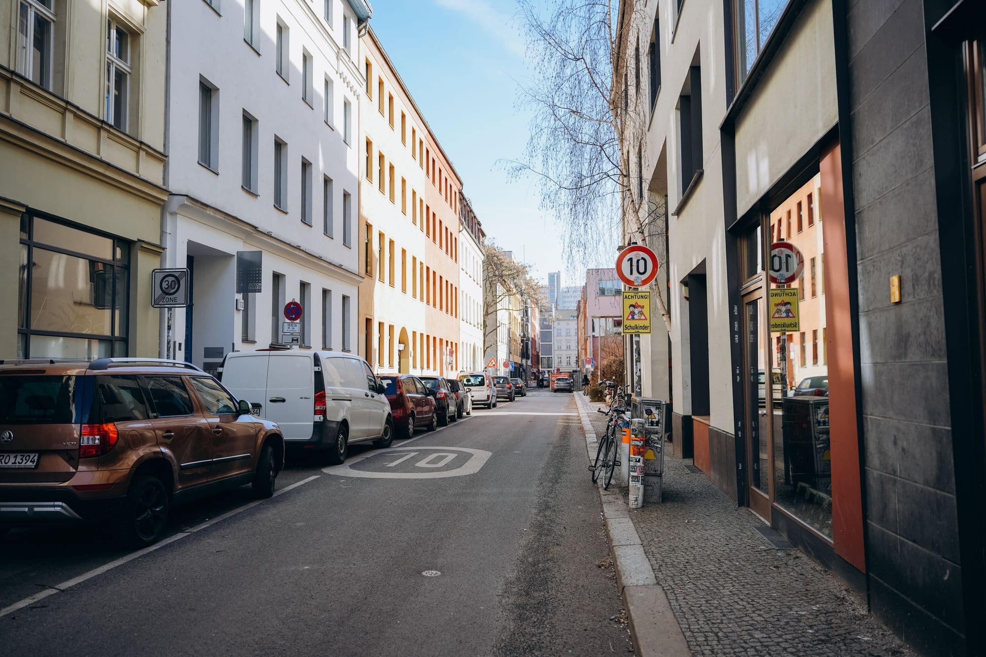 A Berlin street lined with apartment buildings and parked cars in daylight.