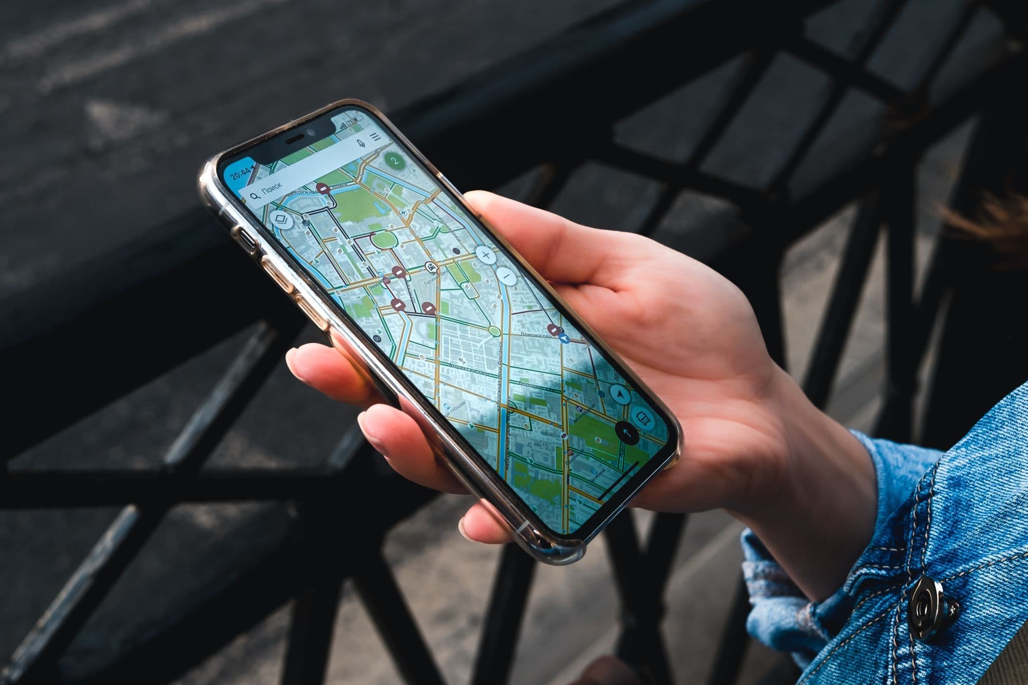 A hand holds a smartphone showing a city map, against a dark metal railing.