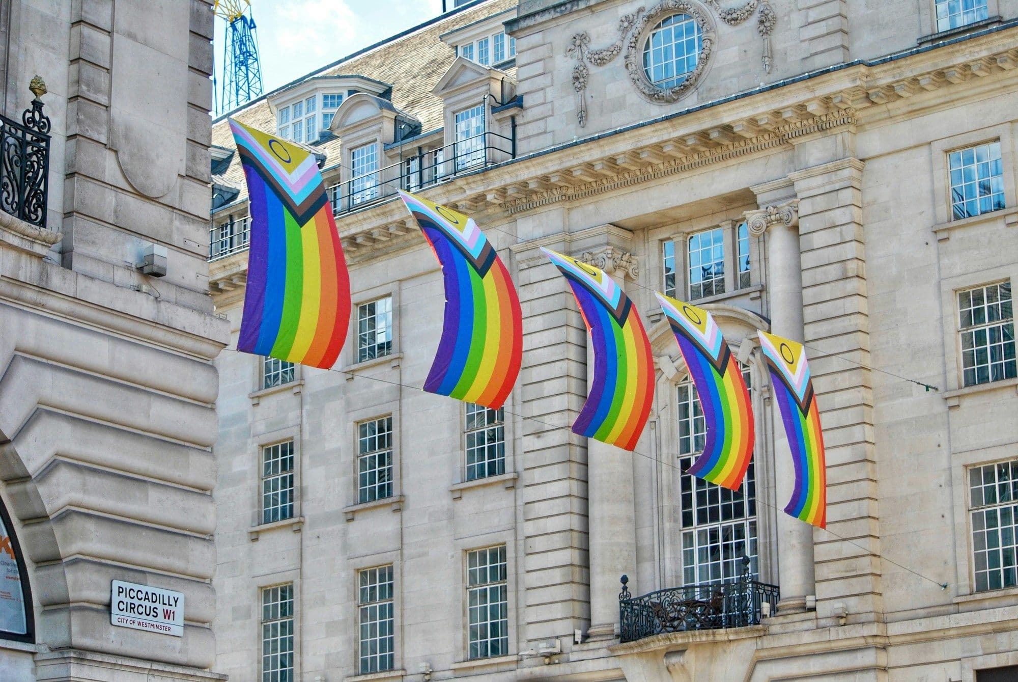 Progress Pride flags hang from the front of a London stone building.