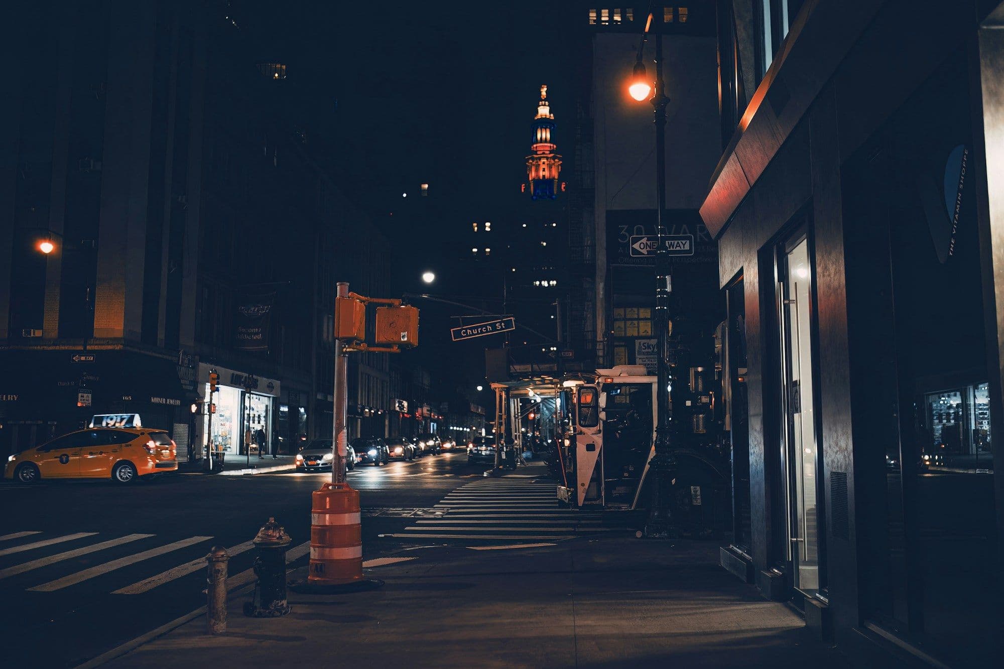 A city street at night with a traffic light and lit shopfronts.