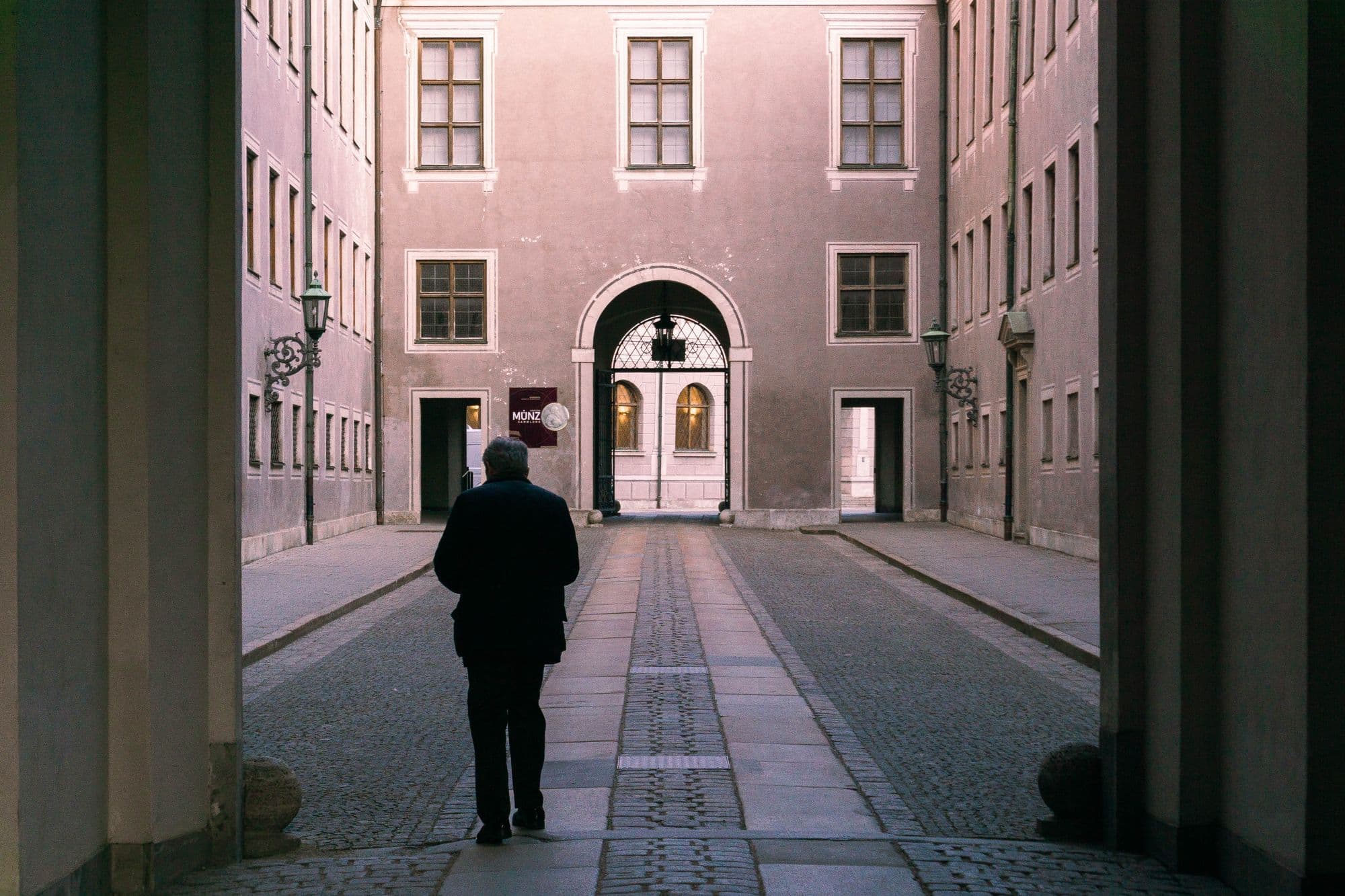A lone traveler walks through a quiet Munich lane framed by historic buildings.