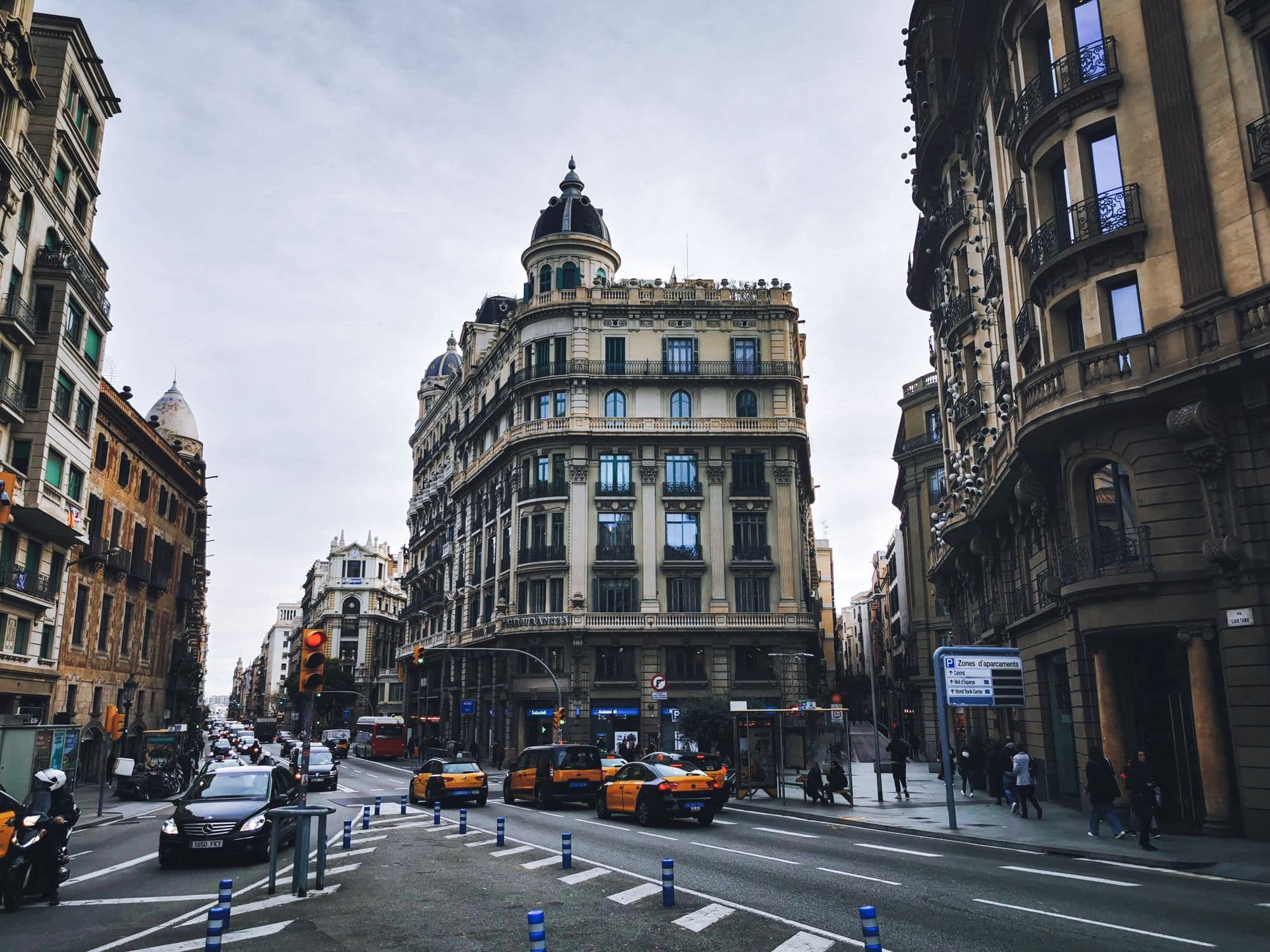 A wide Barcelona intersection with ornate corner buildings, yellow-and-black taxis and a pedestrian crossing.