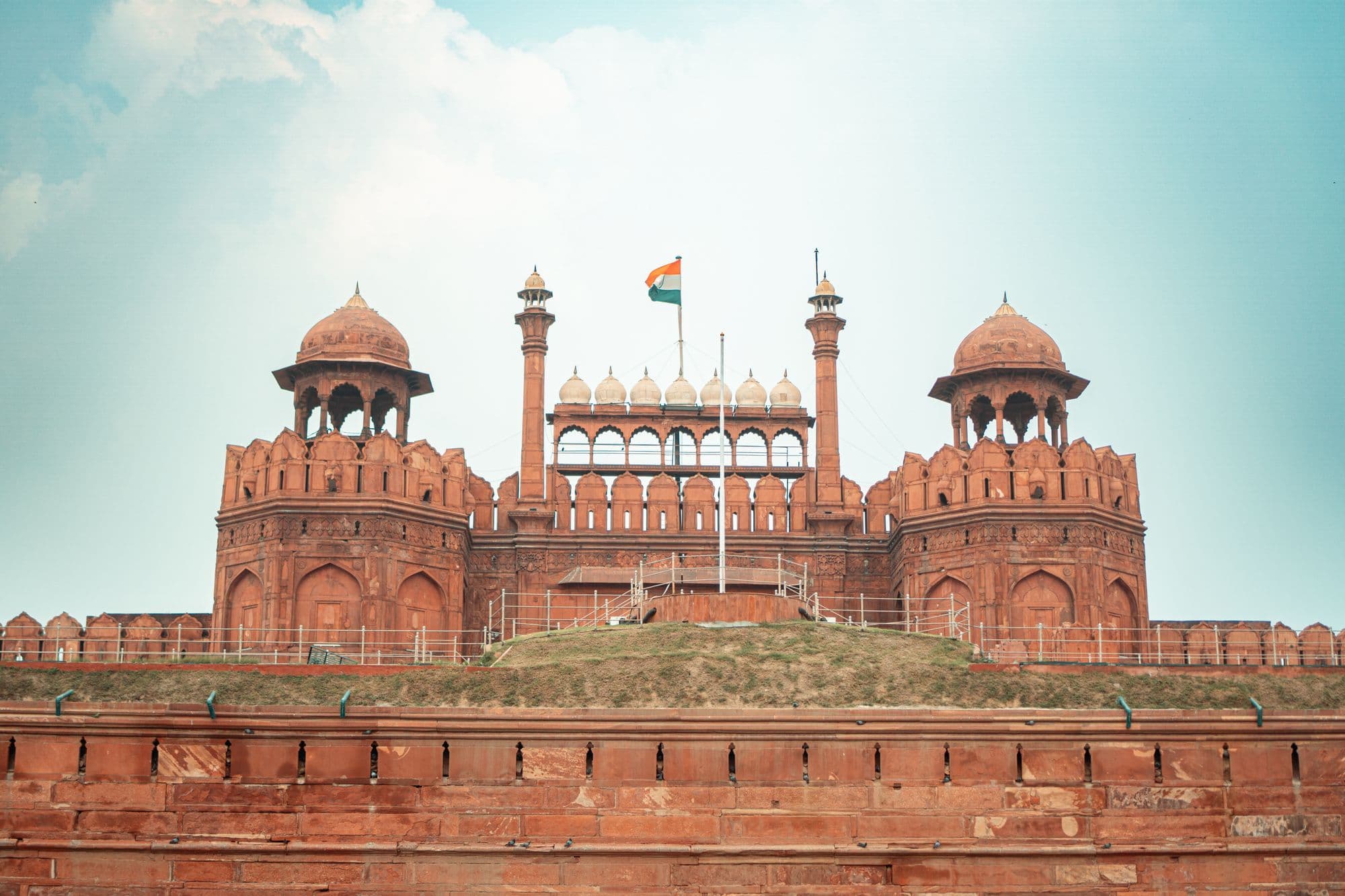 The red sandstone gateway of the Red Fort in Delhi with its domed pavilions and the Indian flag on top.