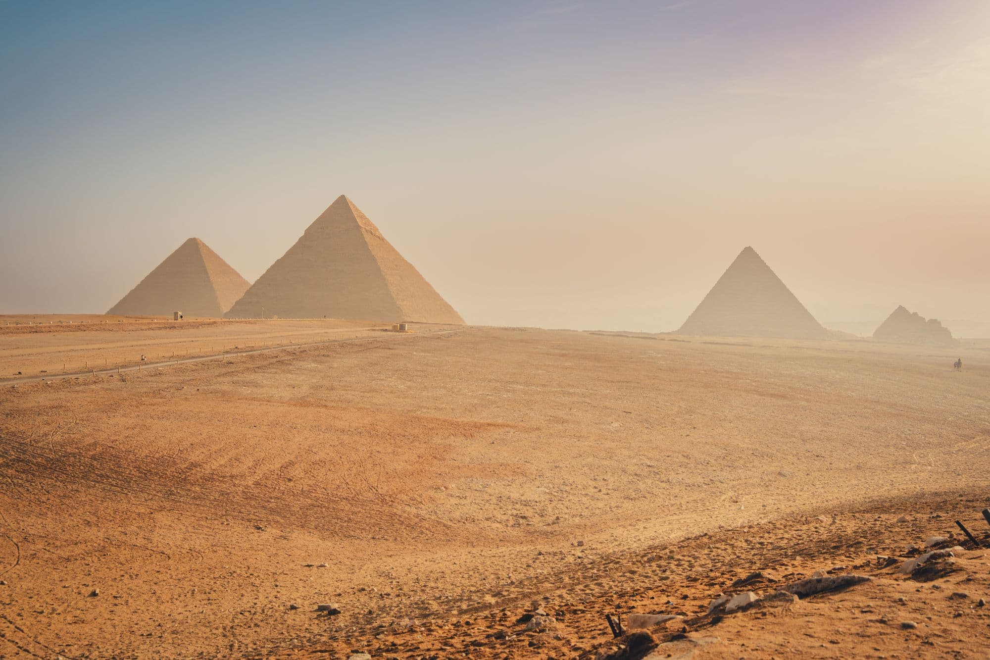Three pyramids of Giza and smaller satellite pyramids standing in pale morning haze across a wide expanse of sand.