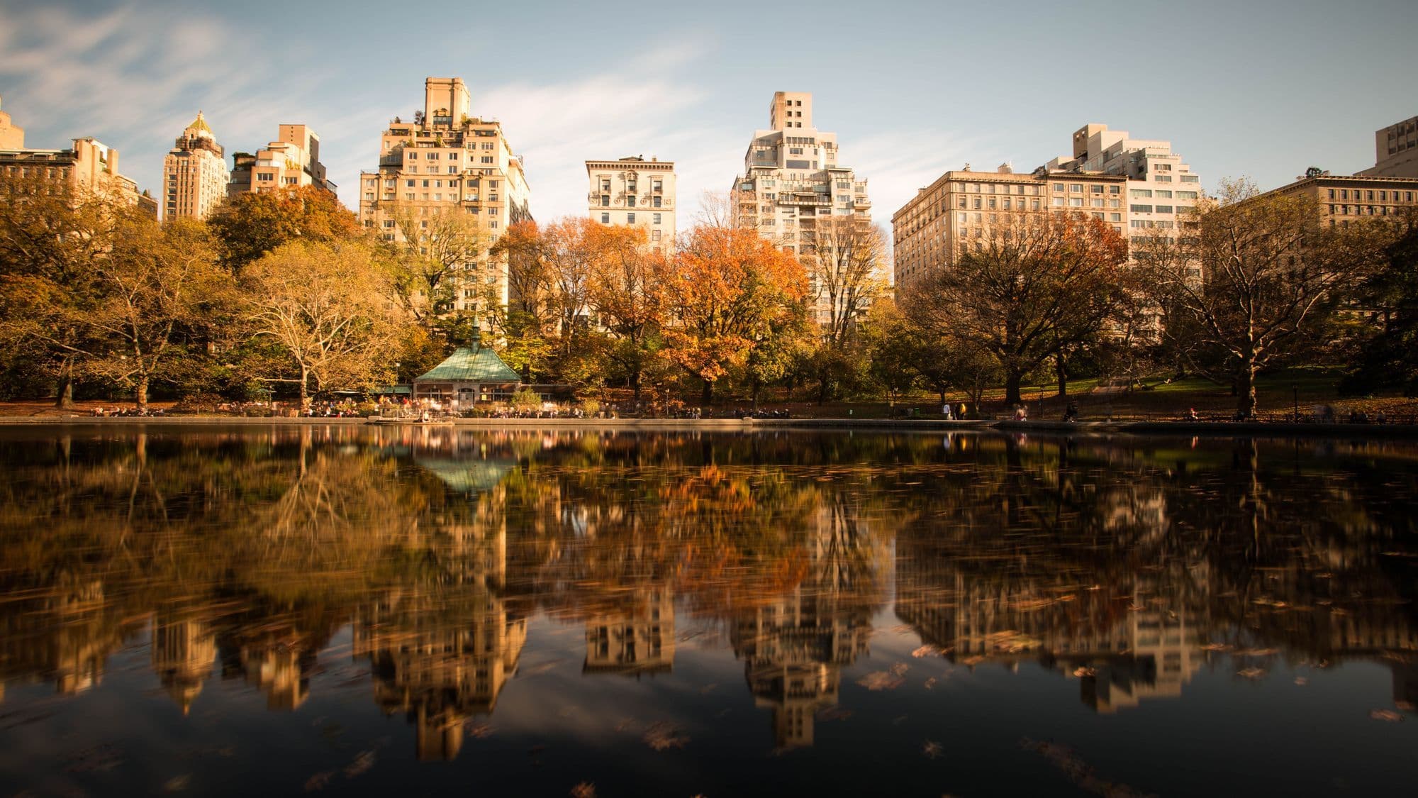 Autumn trees and the Manhattan skyline beside a lake in Central Park.