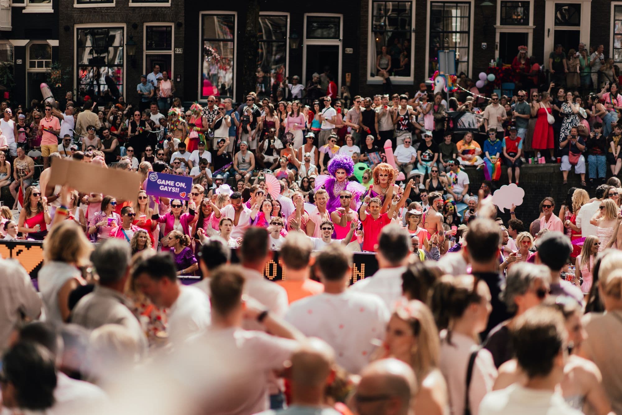 A crowd gathers beside Amsterdam's canal during a sunny Pride celebration.