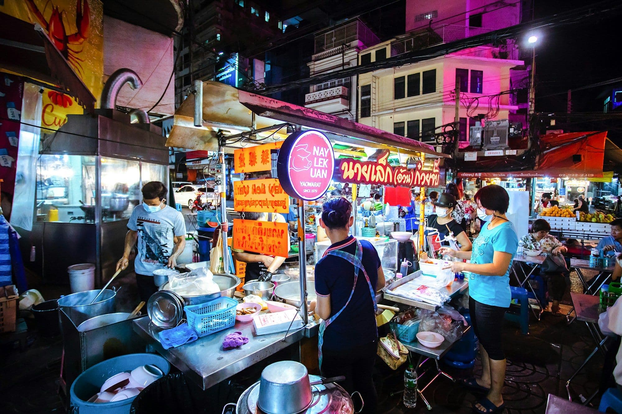 Shoppers move between food stalls in a daytime market.