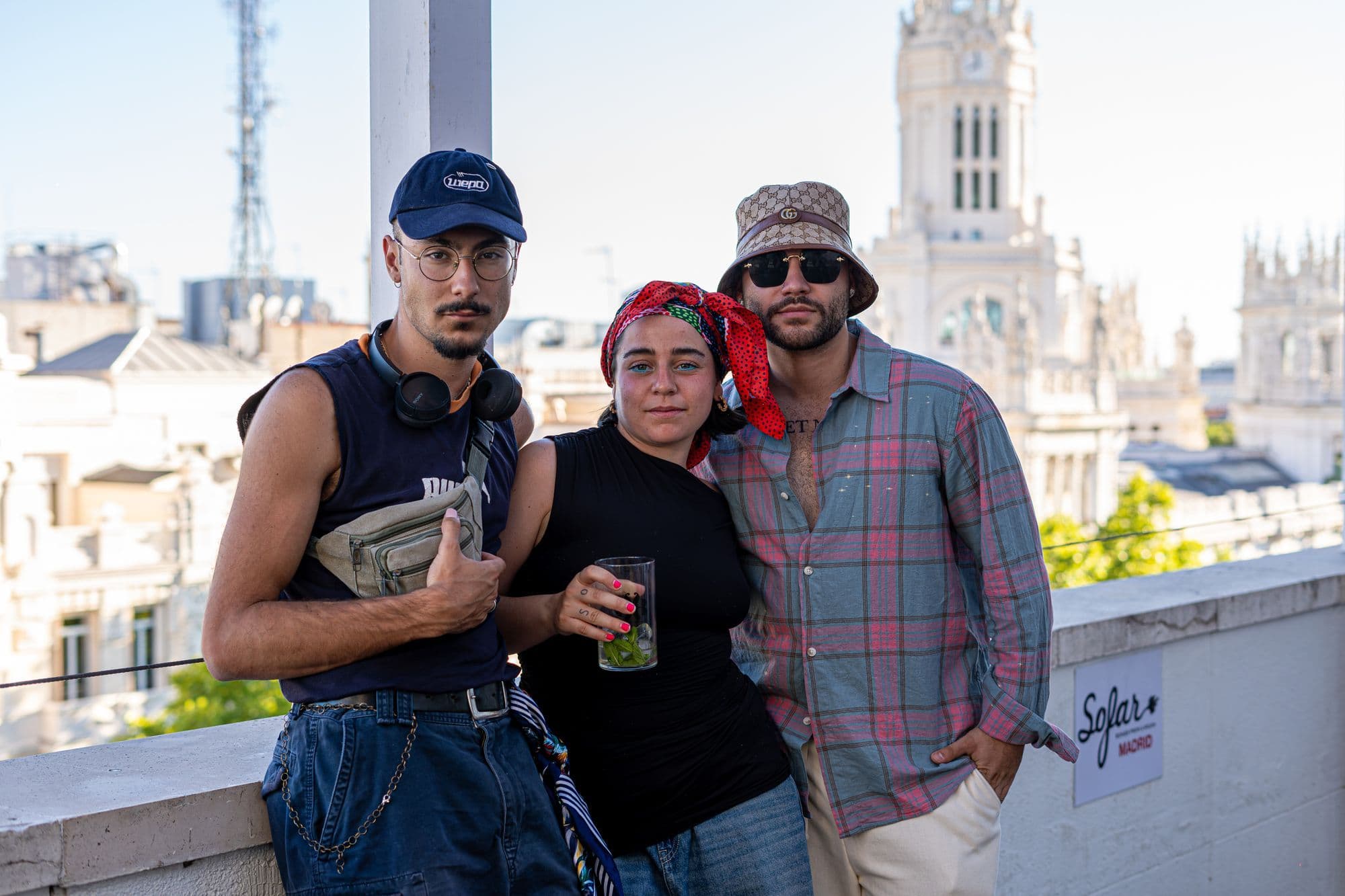 Three friends in sunglasses relax on a Madrid rooftop above the historic centre.