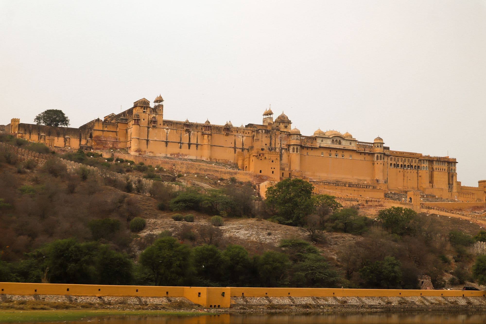 The long honey-coloured walls and palace buildings of Amber Fort on a ridge above a lake near Jaipur.