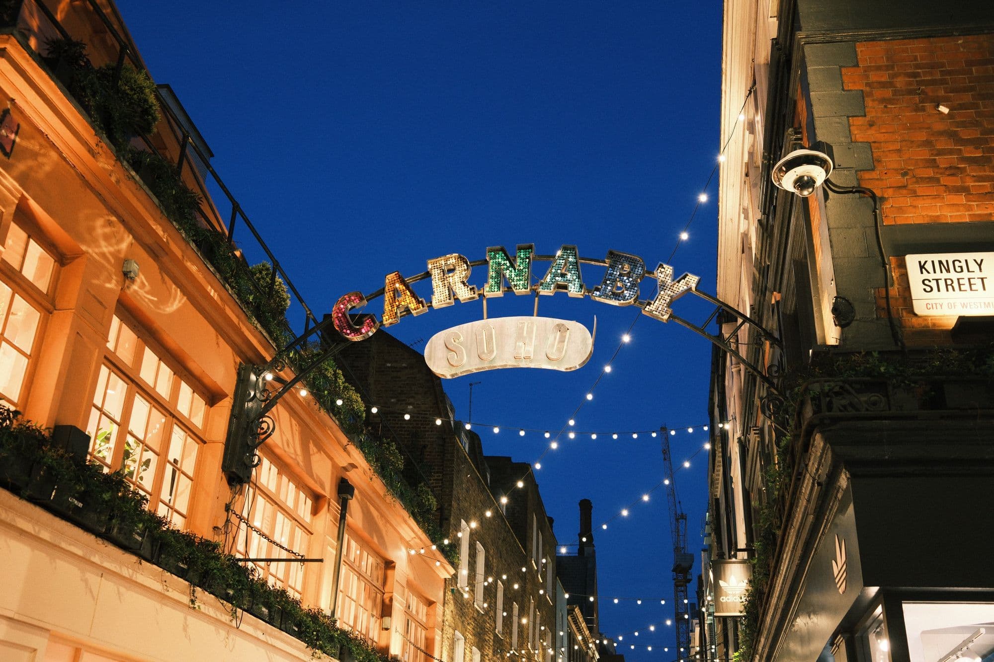Illuminated Carnaby Street arches above pedestrians in Soho after dark.
