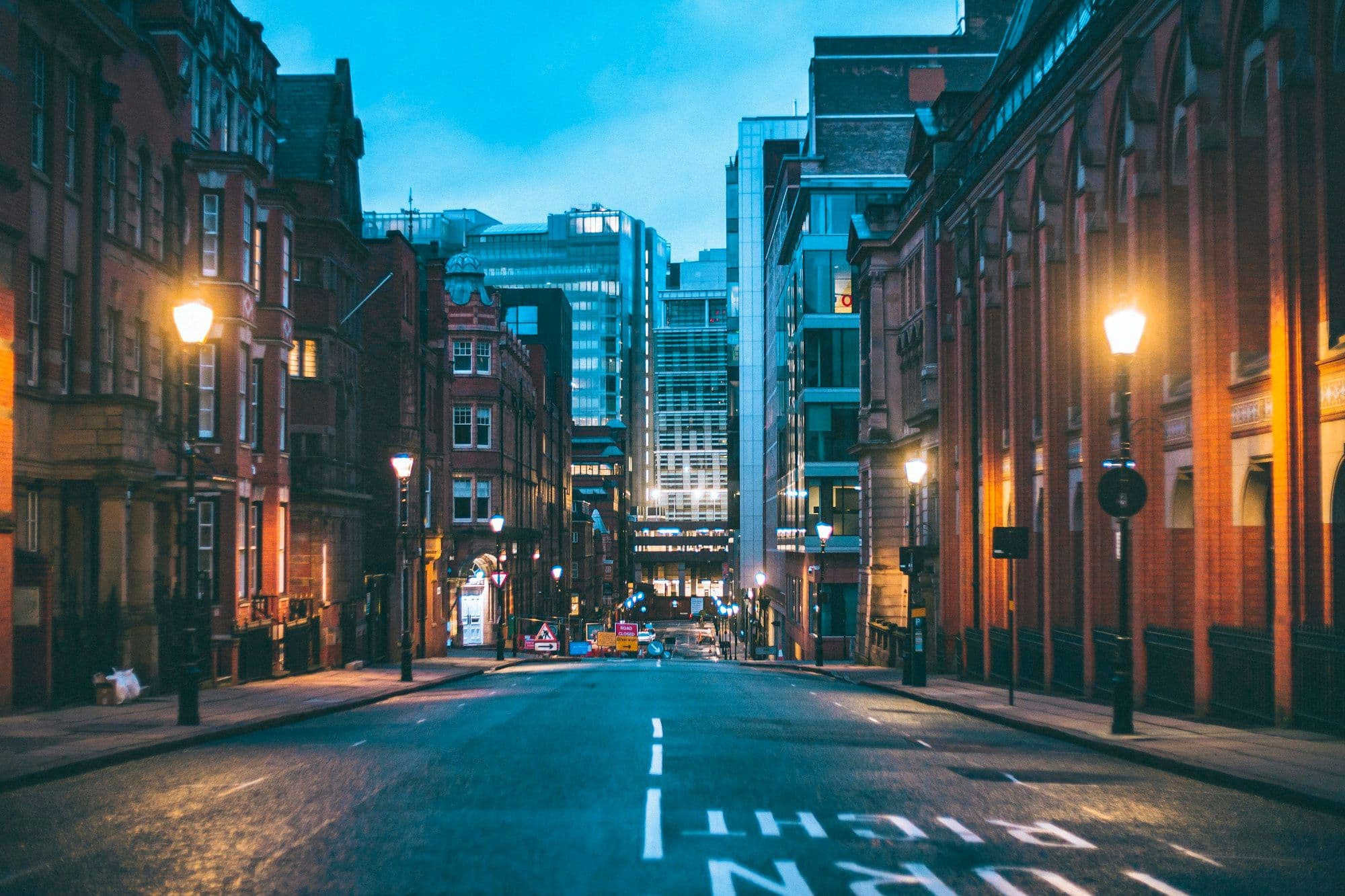 Night traffic moves between tall city buildings under white streetlights.