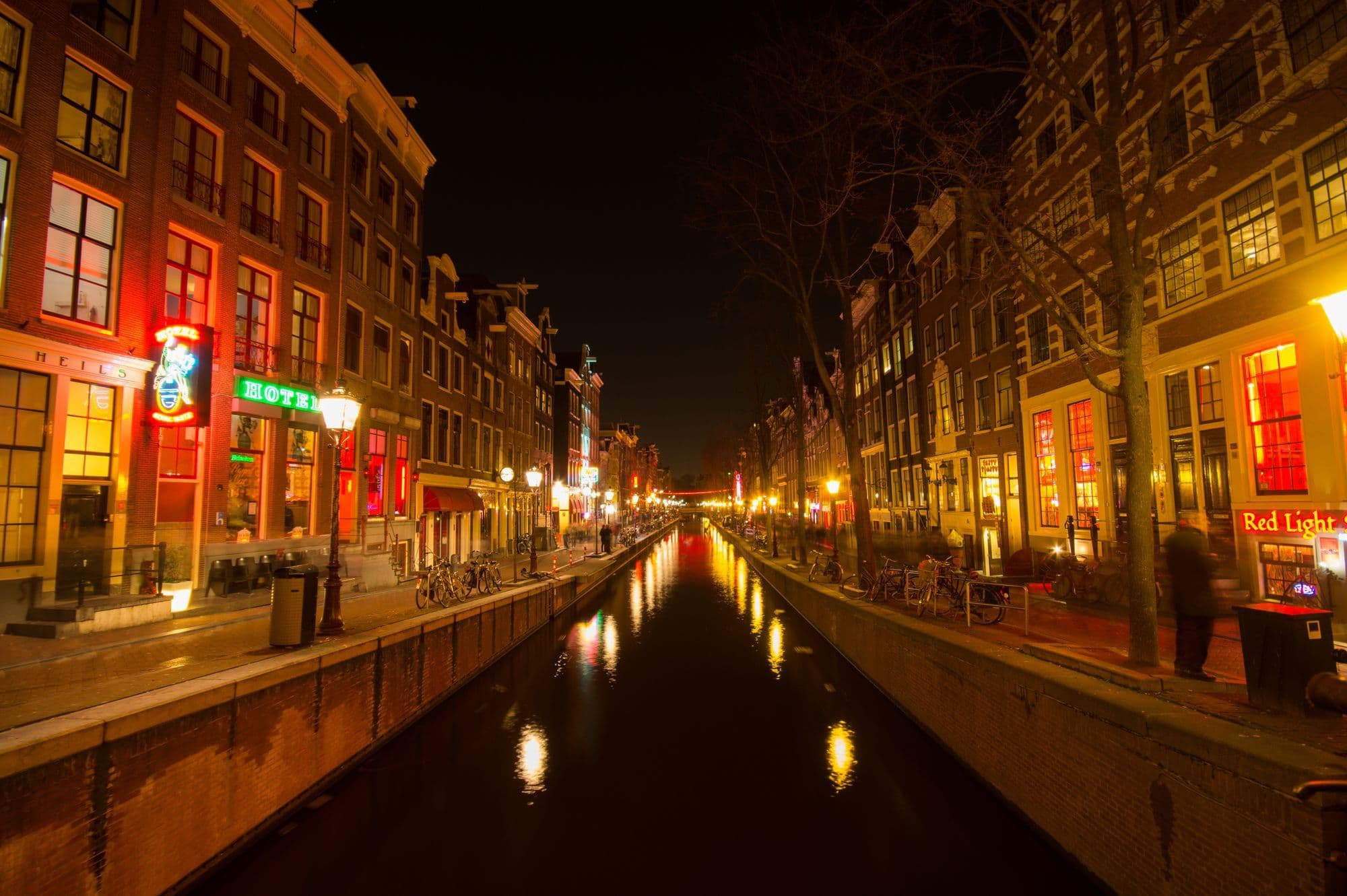 Illuminated canal houses reflect in water on an Amsterdam evening.