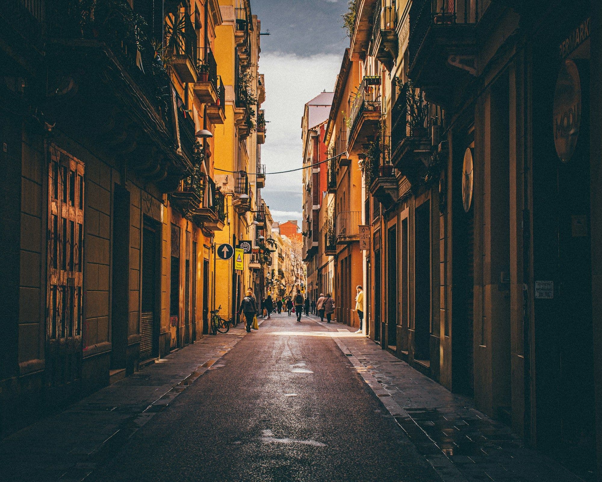 A narrow stone street runs between tall historic buildings in Barcelona's old city.