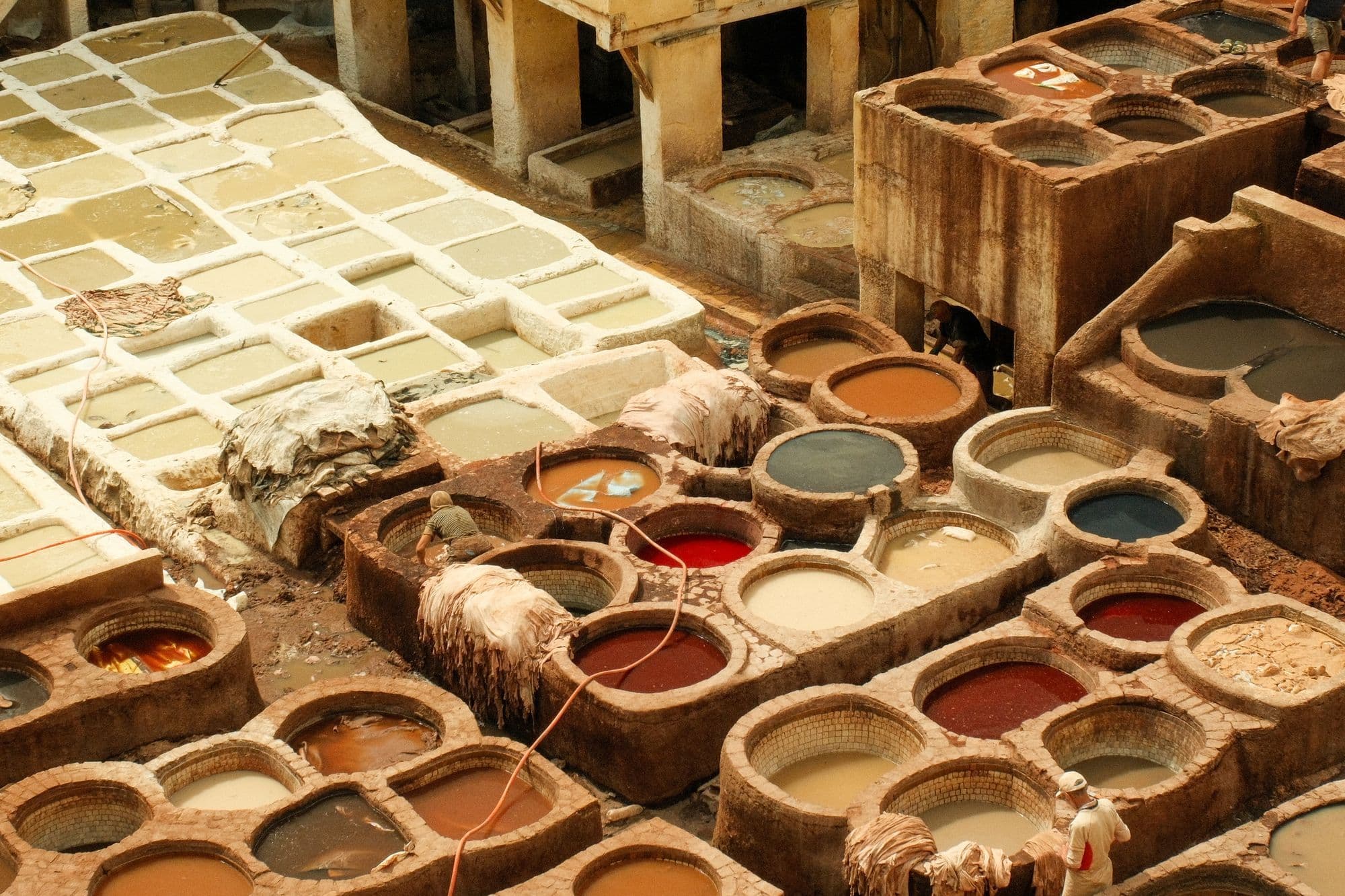 Rows of round stone vats filled with white, brown and red dyes at the Chouara tannery in Fes, seen from above.